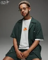 Tatenda  wearing glasses adn a white t-shirt with a dark green shirt over the top