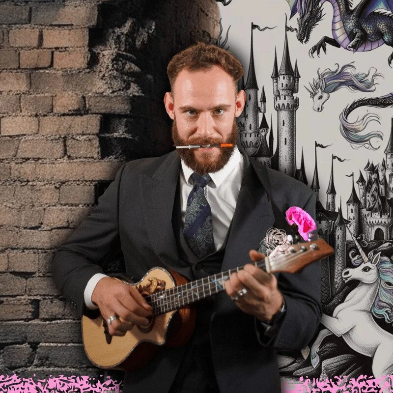Troy in a suit and tie in front of a half brick, half fantasy illustration background with a capped needle clenched vertically beteween his teeth, playing a small guitar