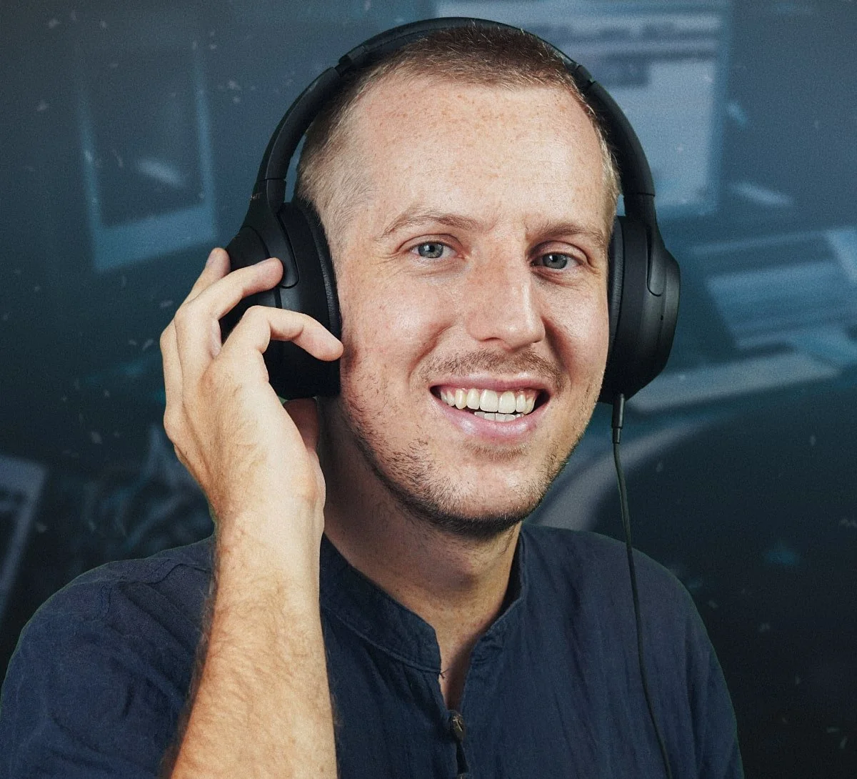 A young man with short hair and light skin smiles and wears over-ear headphones.