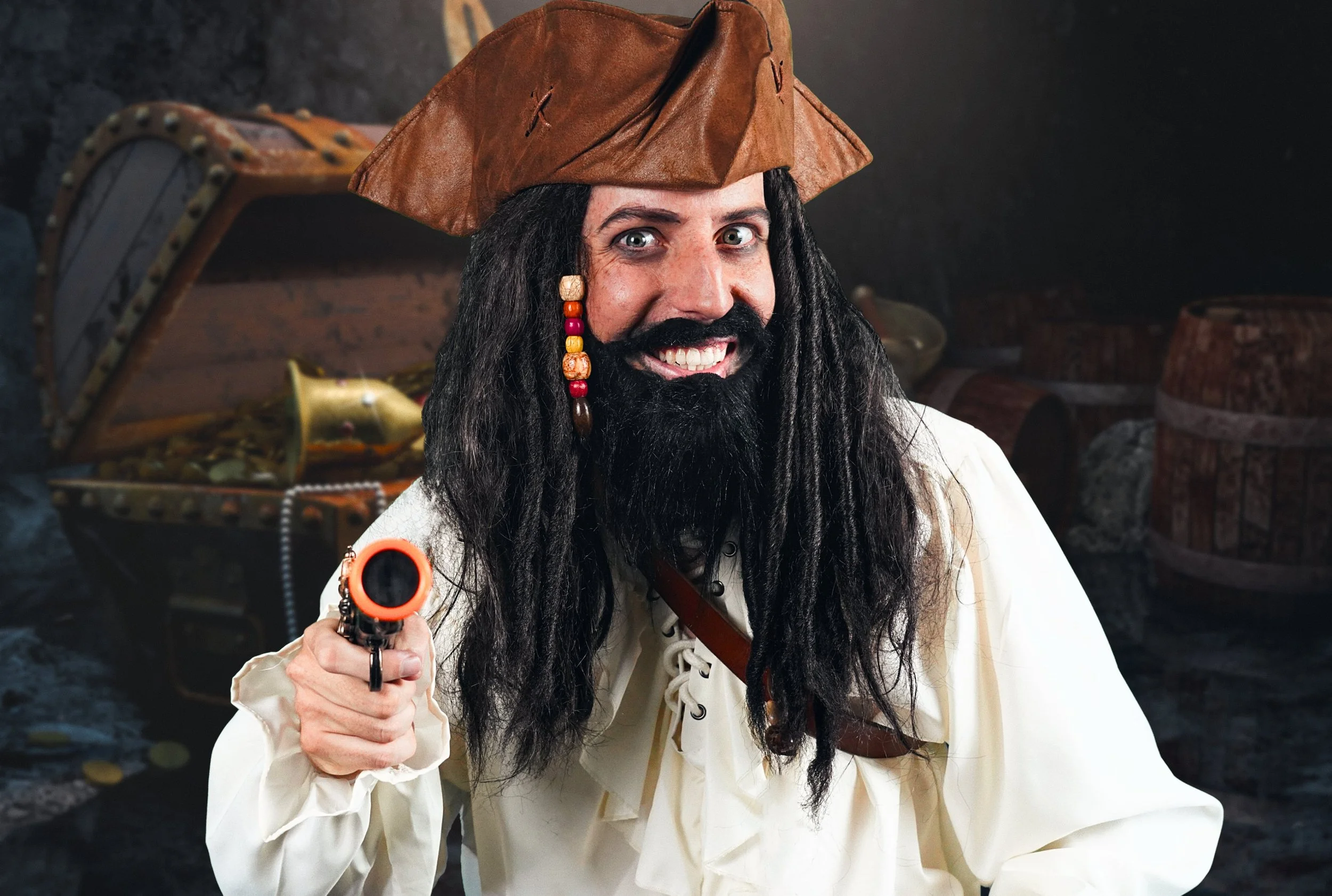 Person dressed as a pirate with a brown tricorn hat, long black beard, and braids with beads, pointing a toy pistol, with a background of treasure chests and gold coins.