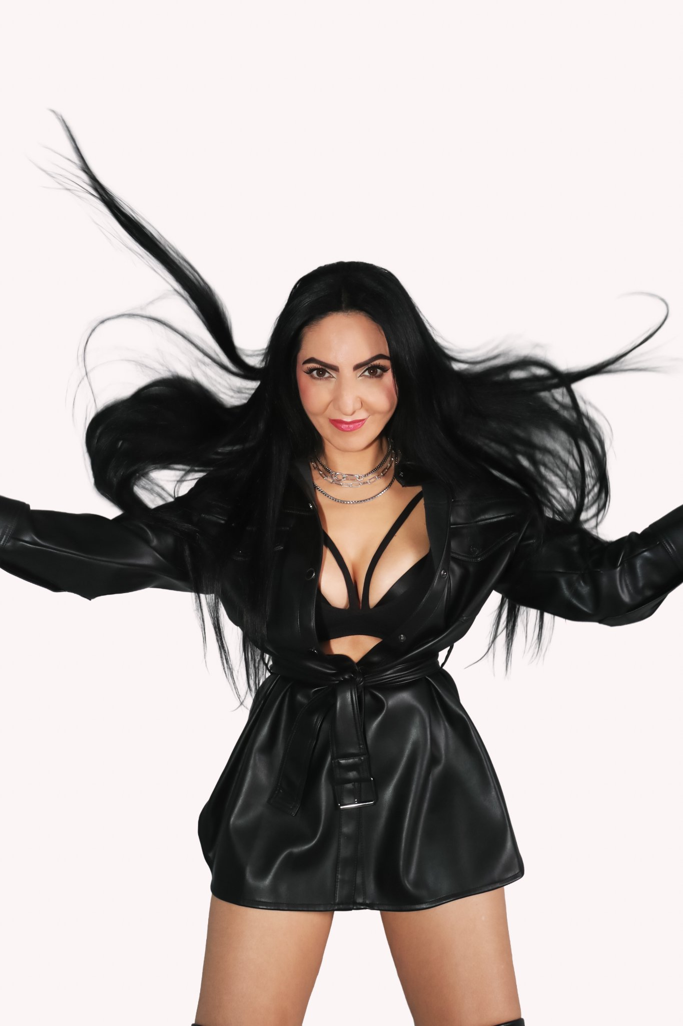 Woman in black leather jacket and skirt, smiling, with flowing black hair against a plain white background.
