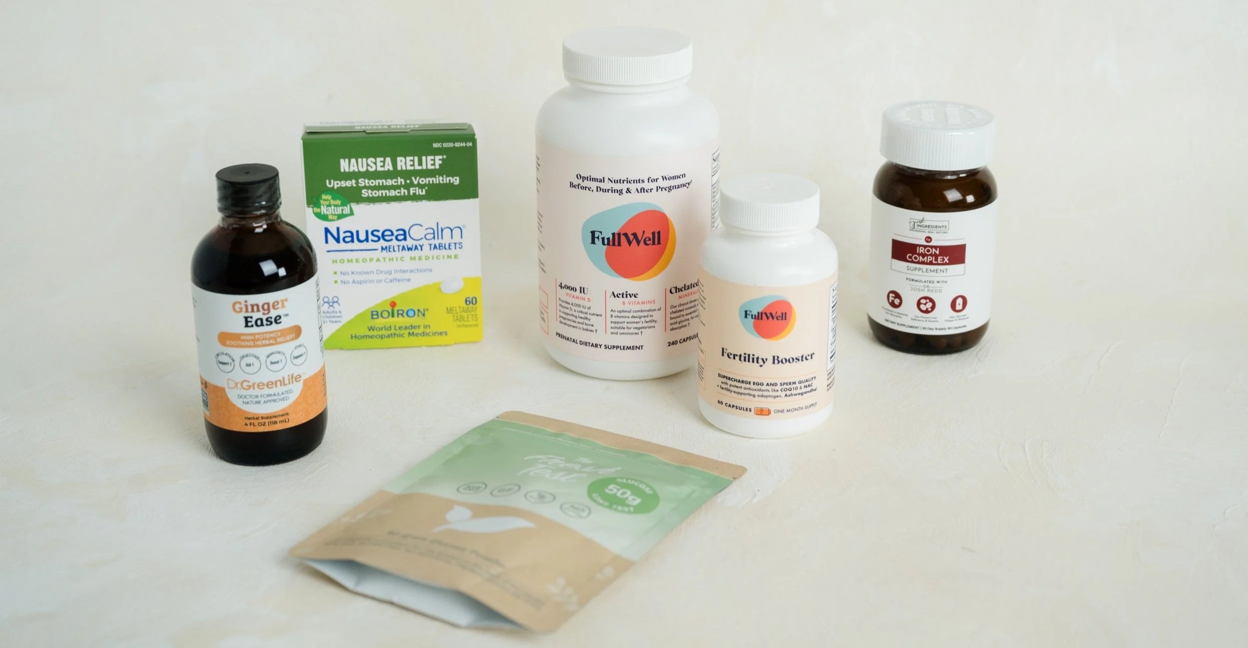 Assorted health supplements including ginger extract, nausea relief tablets, prenatal vitamins, fertility booster, iron supplement, and a herbal packet, all on a light-colored surface.