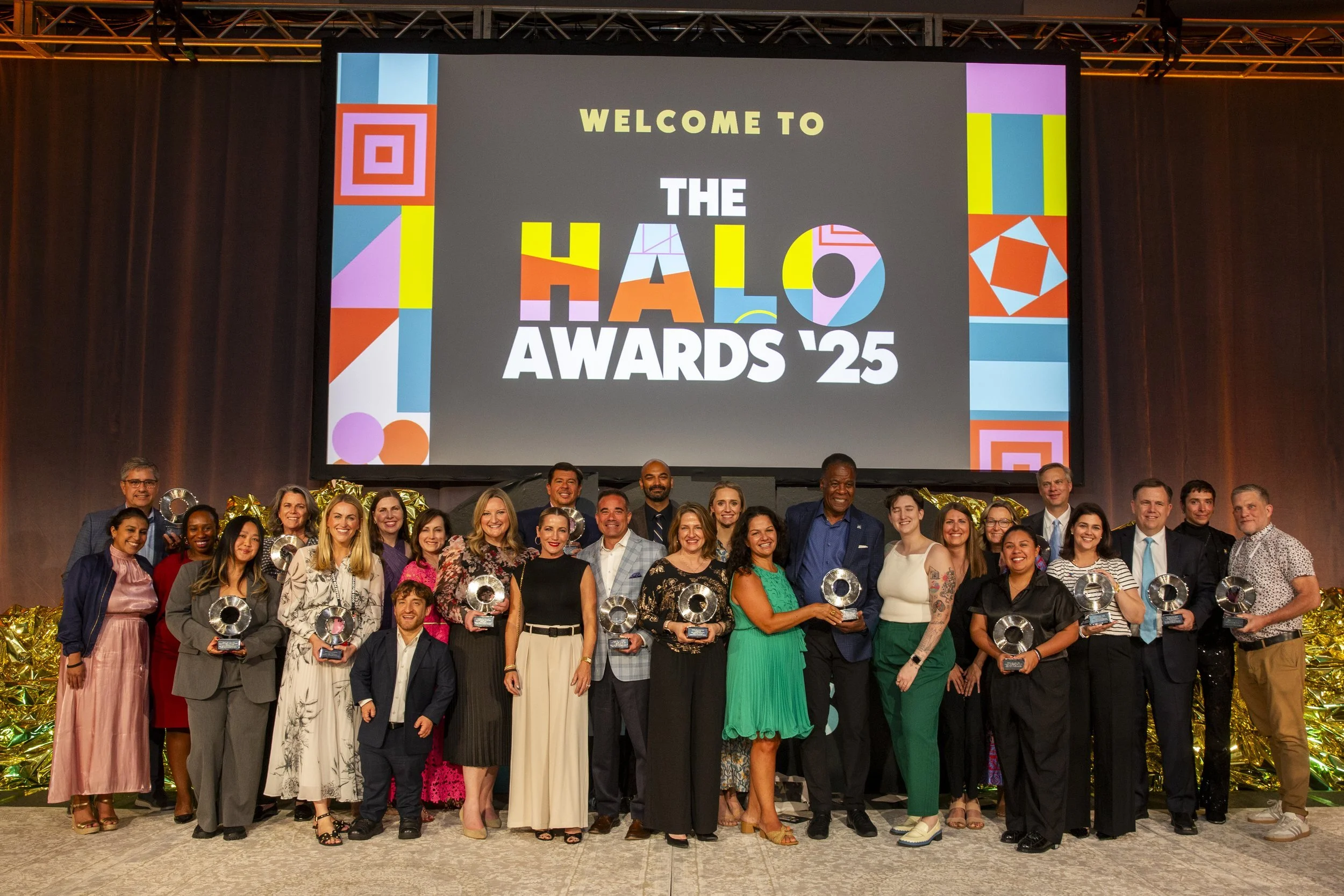 Group of people at the Halo Awards 2025 holding awards in front of a large screen that displays the event logo and name.