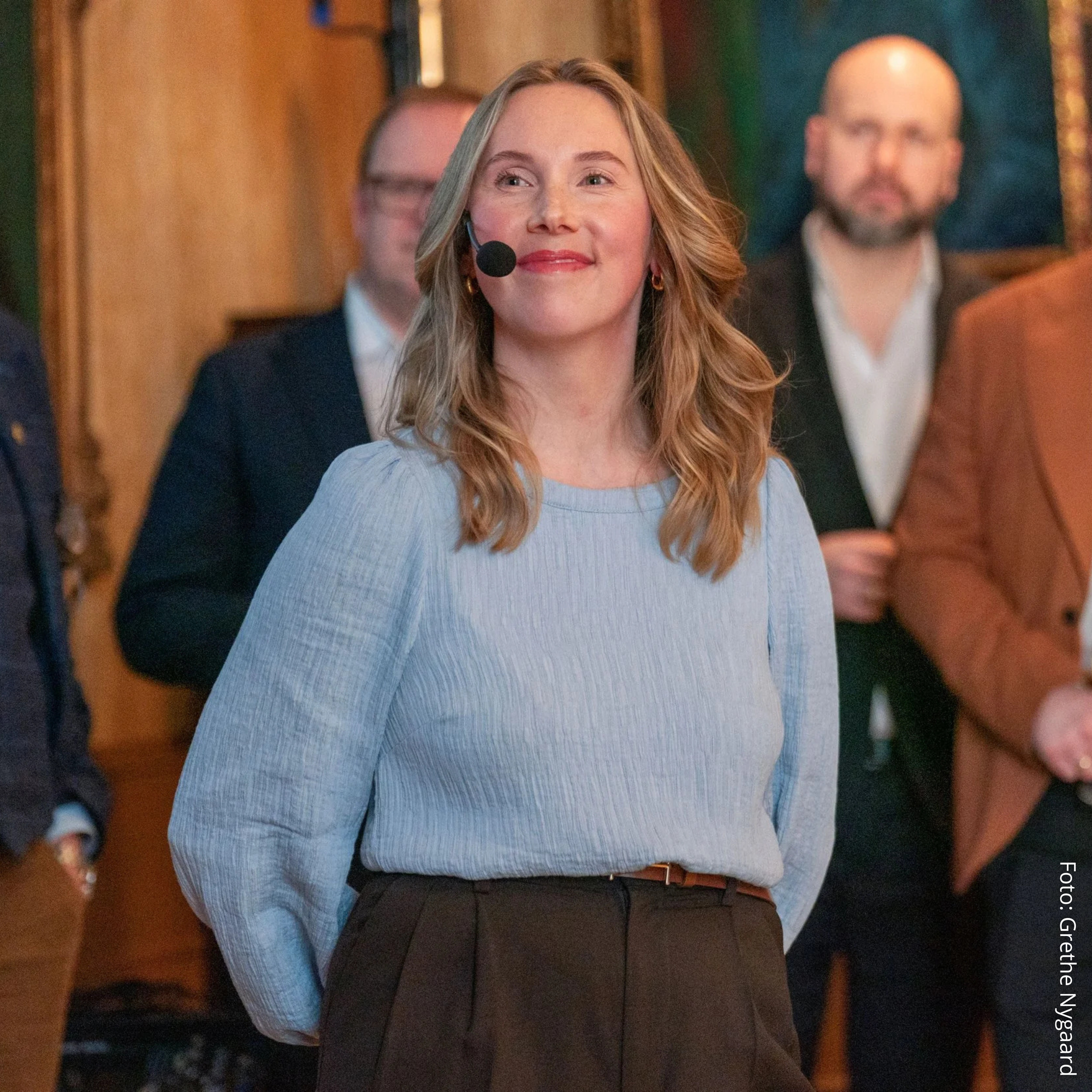 En kvinne smiler mens hun har på seg mikrofon på et arrangement.