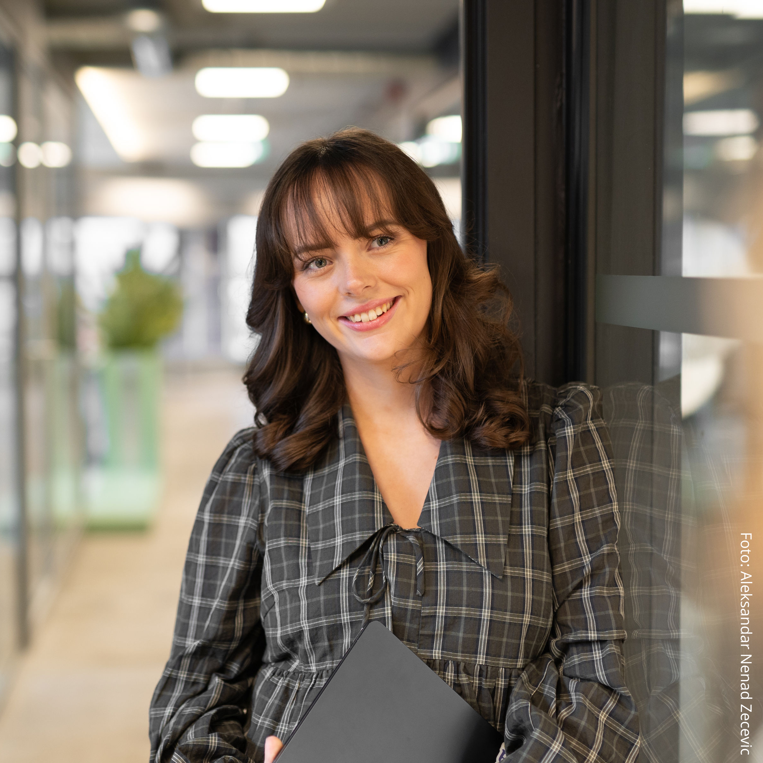 En kvinne smiler mens hun holder en laptop i en kontorgang