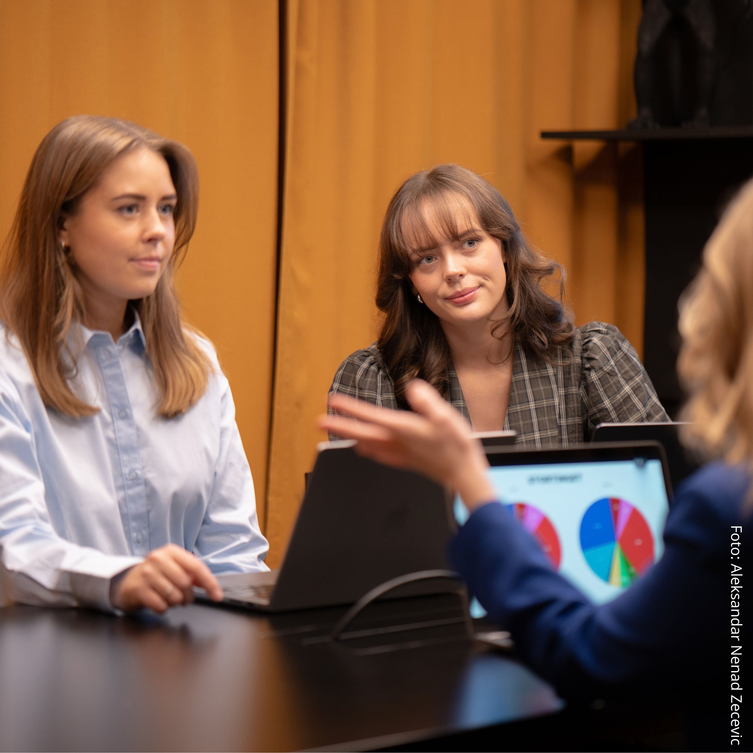 Tre kvinner i et moderne møterom som diskuterer og ser på statistikk.