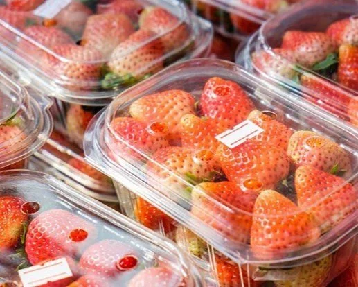 Clear plastic containers filled with fresh strawberries on a store shelf.