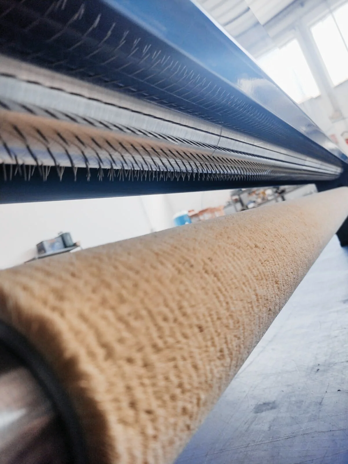 Close-up of an industrial machine with metal teeth and a brown textured roller underneath, in a factory or workshop setting.