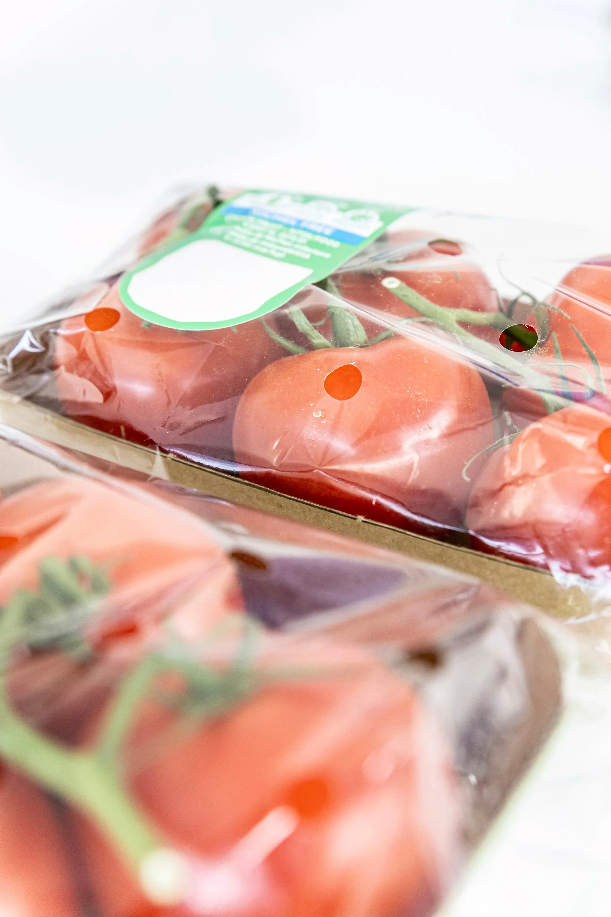 A plastic container of cherry tomatoes with green stems, partially covered with plastic wrap and a green label.