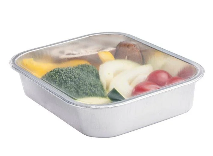 A meal in a metal container with vegetables including broccoli, cherry tomatoes, onions, and yellow bell pepper, covered with a clear plastic lid.