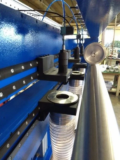Close-up of industrial machinery with blue metal frame and black components connected to a silver cylindrical pipe and flexible hoses.