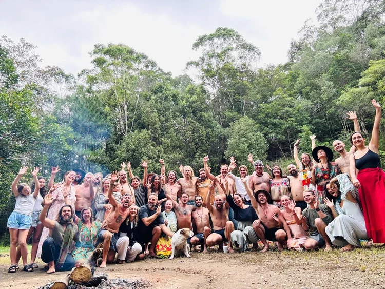 Community group smiling and raising their arms beside a forest