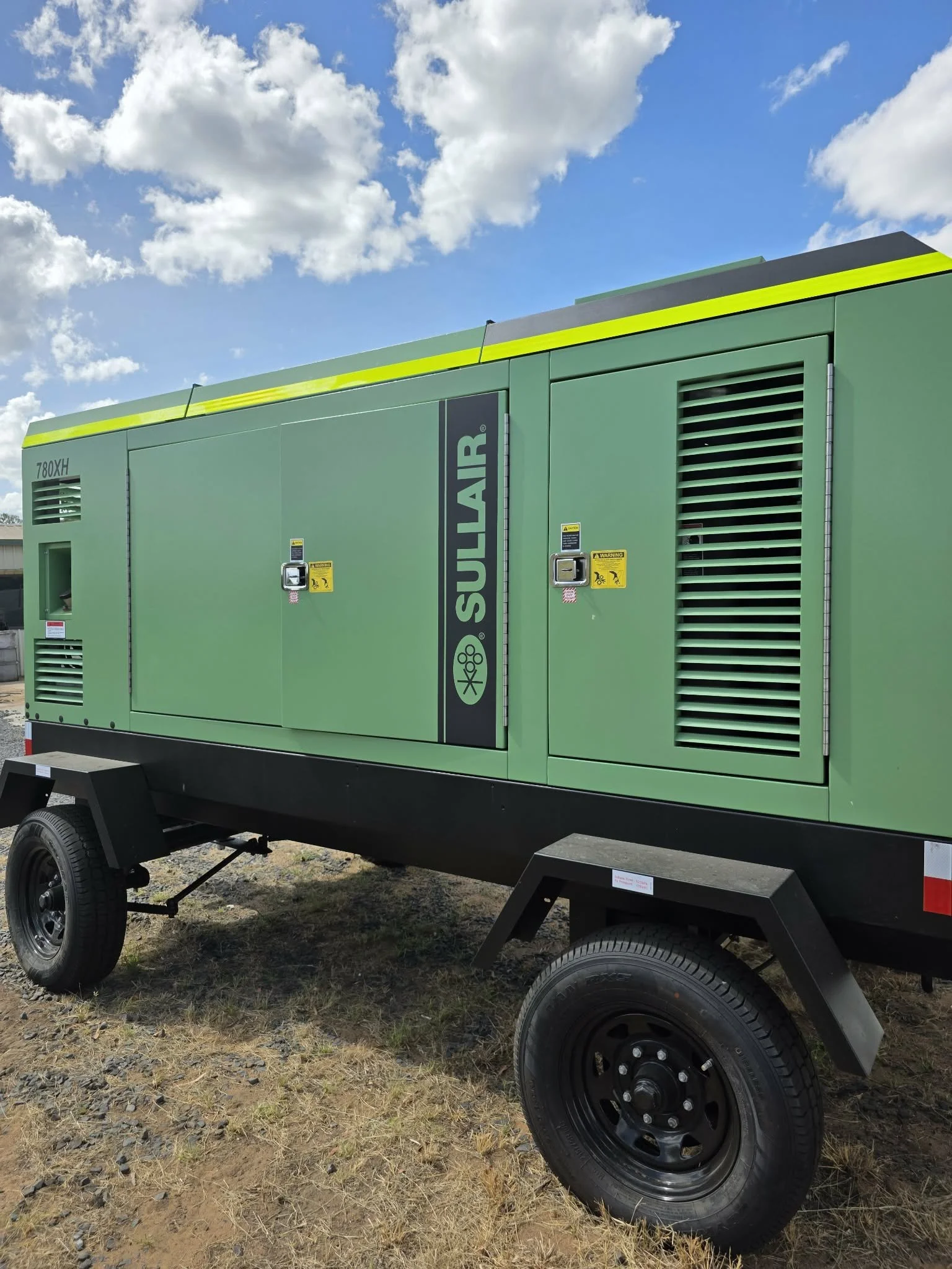 A large green portable generator on wheels outdoors, with a cloudy sky in the background.