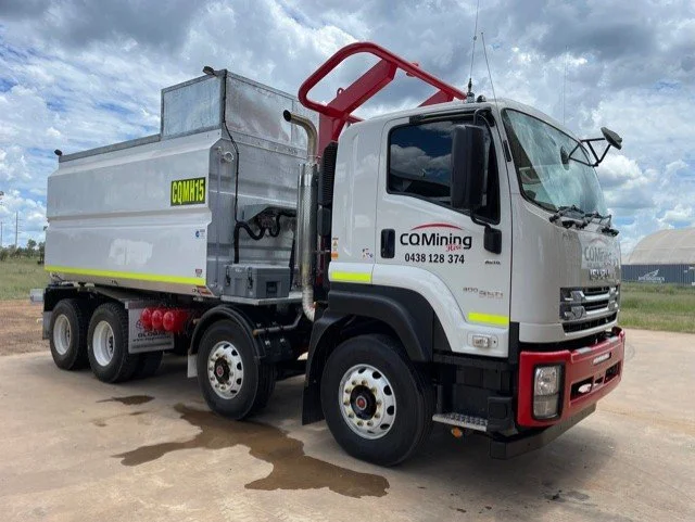 Mining truck labeled 'COMING' with a company phone number, parked outdoors on a cloudy day.