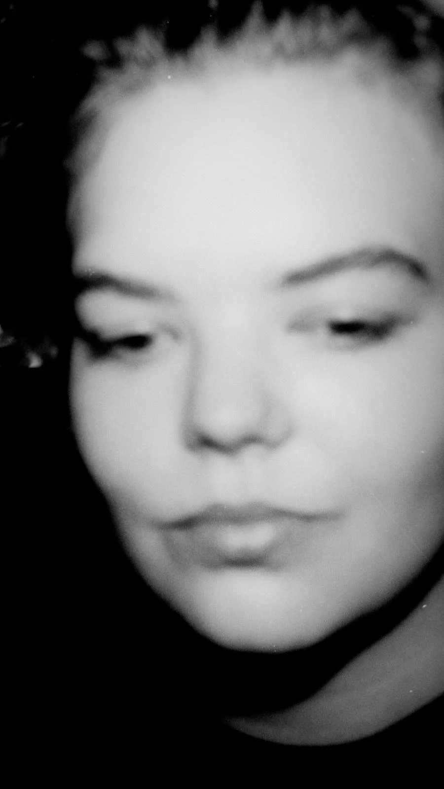 Schwarz-weiß-Foto eines Gesichts mit geschlossenen Augen, lockigem Haar und vollen Lippen.