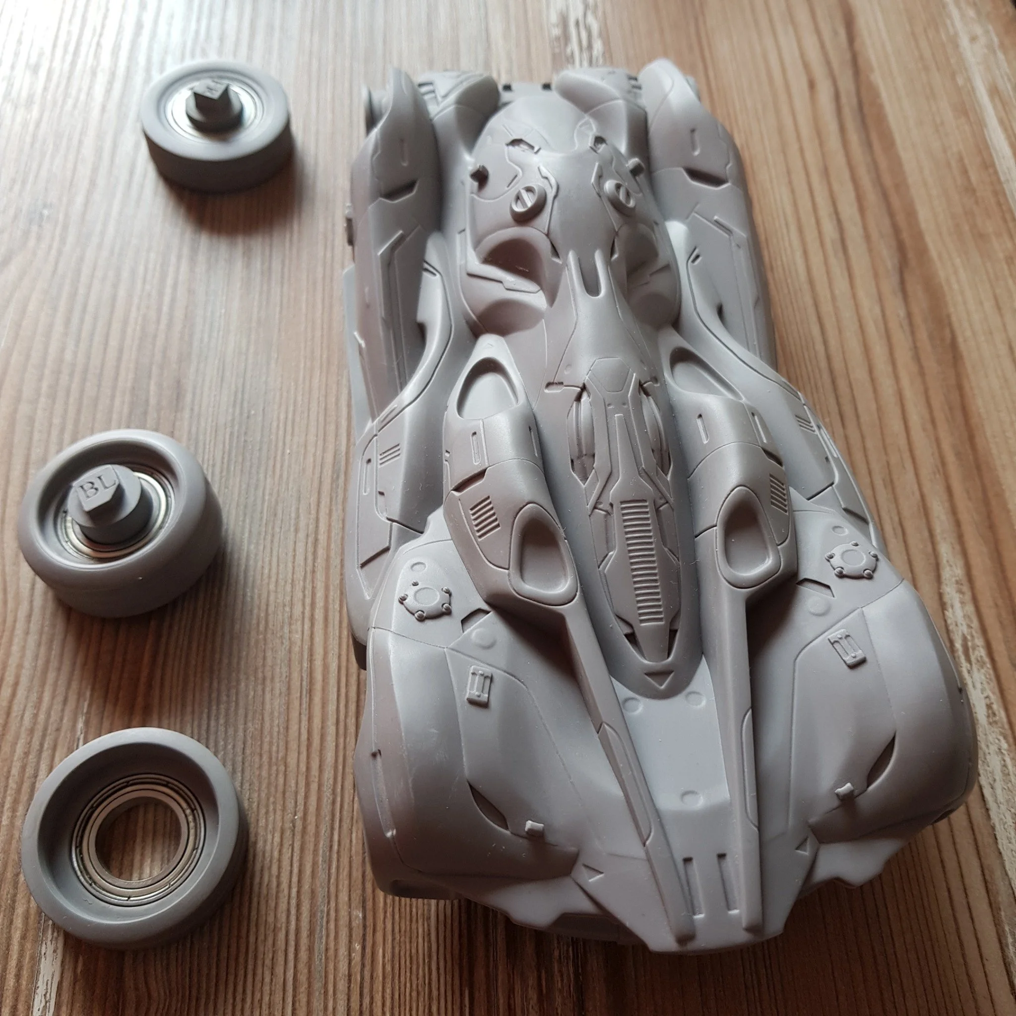 A gray model of a spaceship with three wheels on a wooden surface.