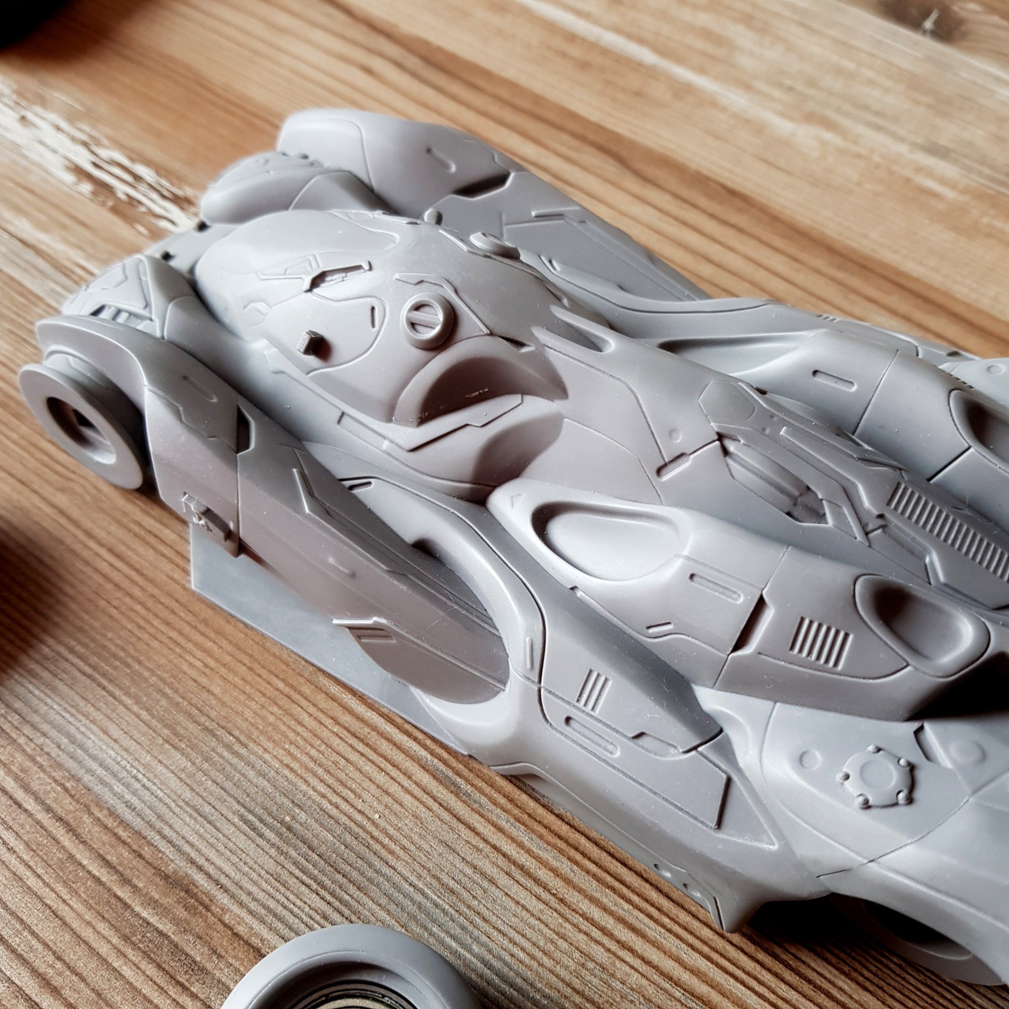 A detailed gray model spaceship with intricate surface design, resting on a wooden surface.