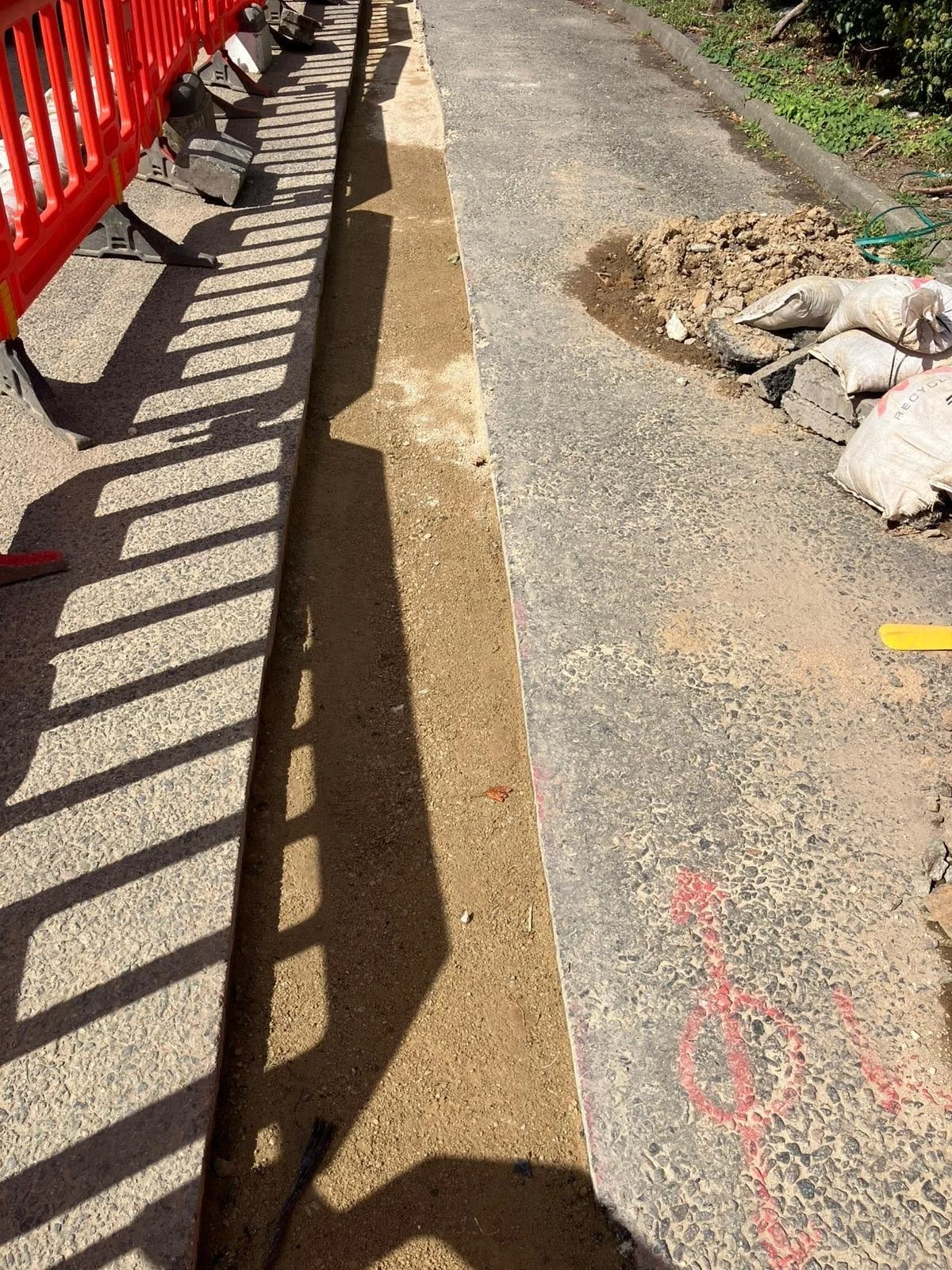 Construction site sidewalk with barrier, dirt, and paving materials.