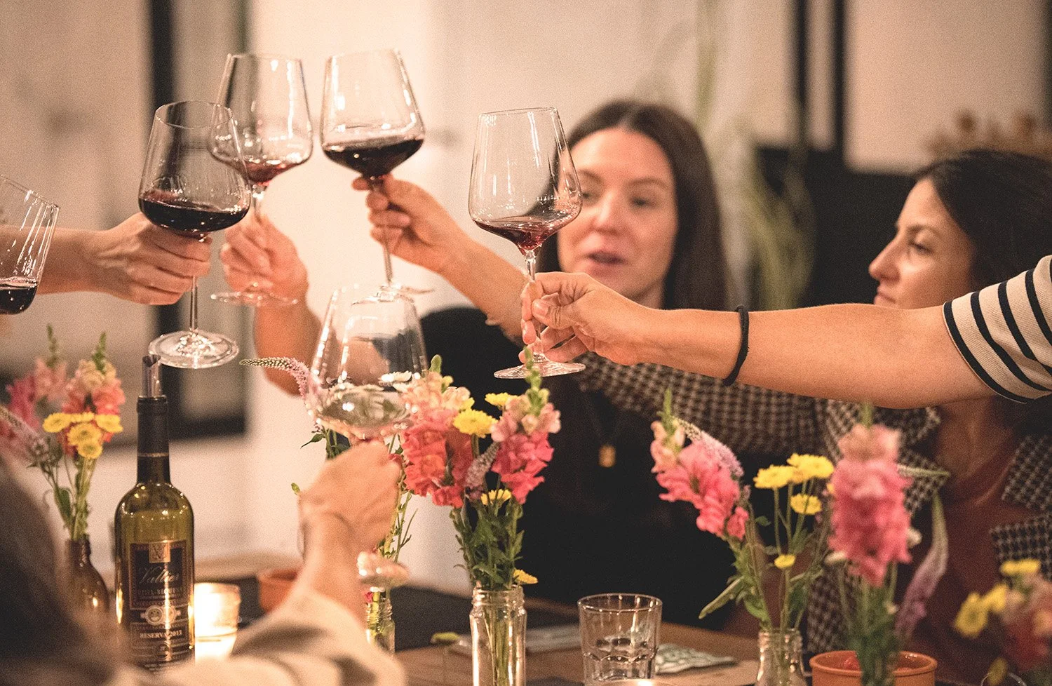 Grupo de personas brindando con copas de vino en una cena con flores decorativas.