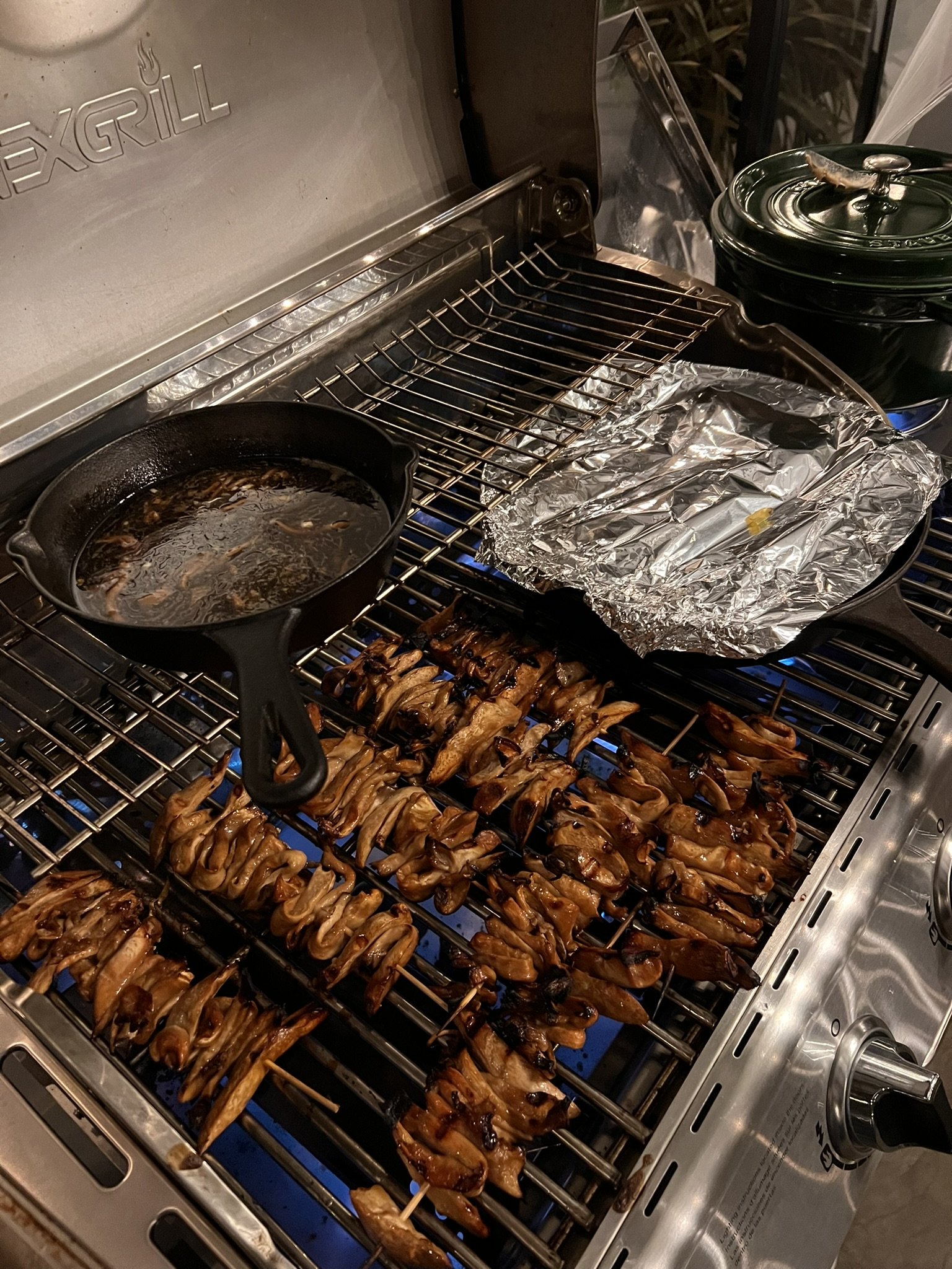 Churrasco de pollo en la parrilla, con una olla de cocción, papel de aluminio y una olla de olla de cocción lenta en una parrilla de gas.