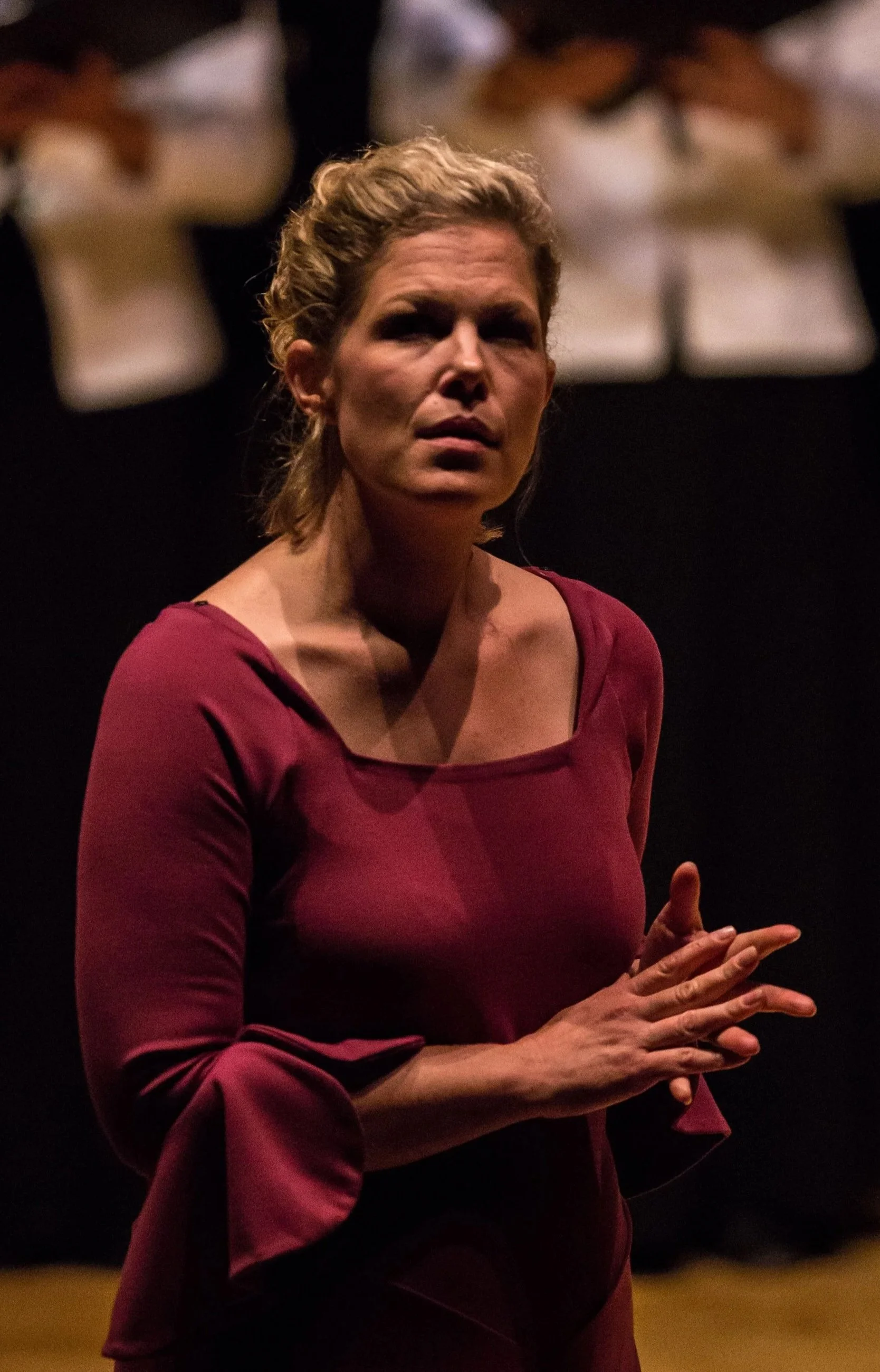 woman standing on stage with hands together and people behind her