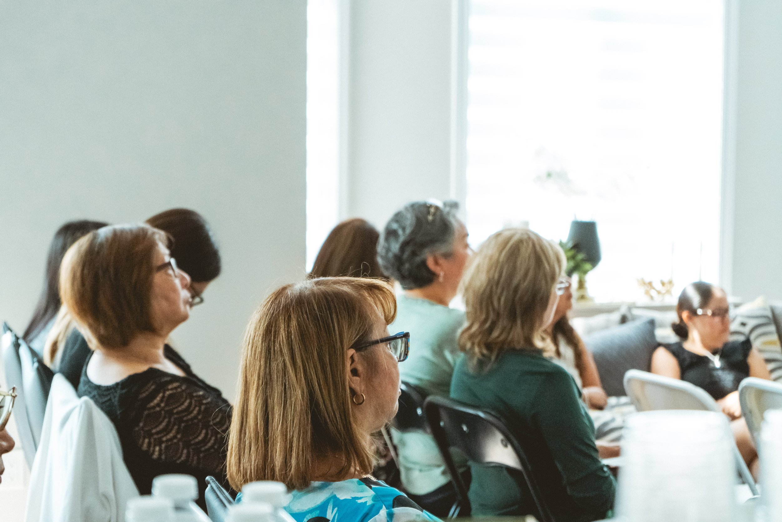 Group of people sitting and listening attentively in a well-lit room, likely attending a seminar or workshop.