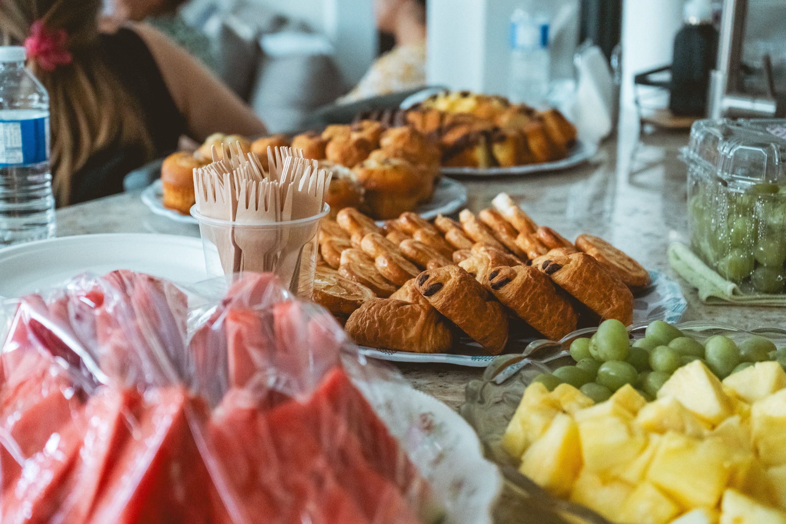 Table with pastries, watermelon, pineapple, grapes, water bottle, and forks.