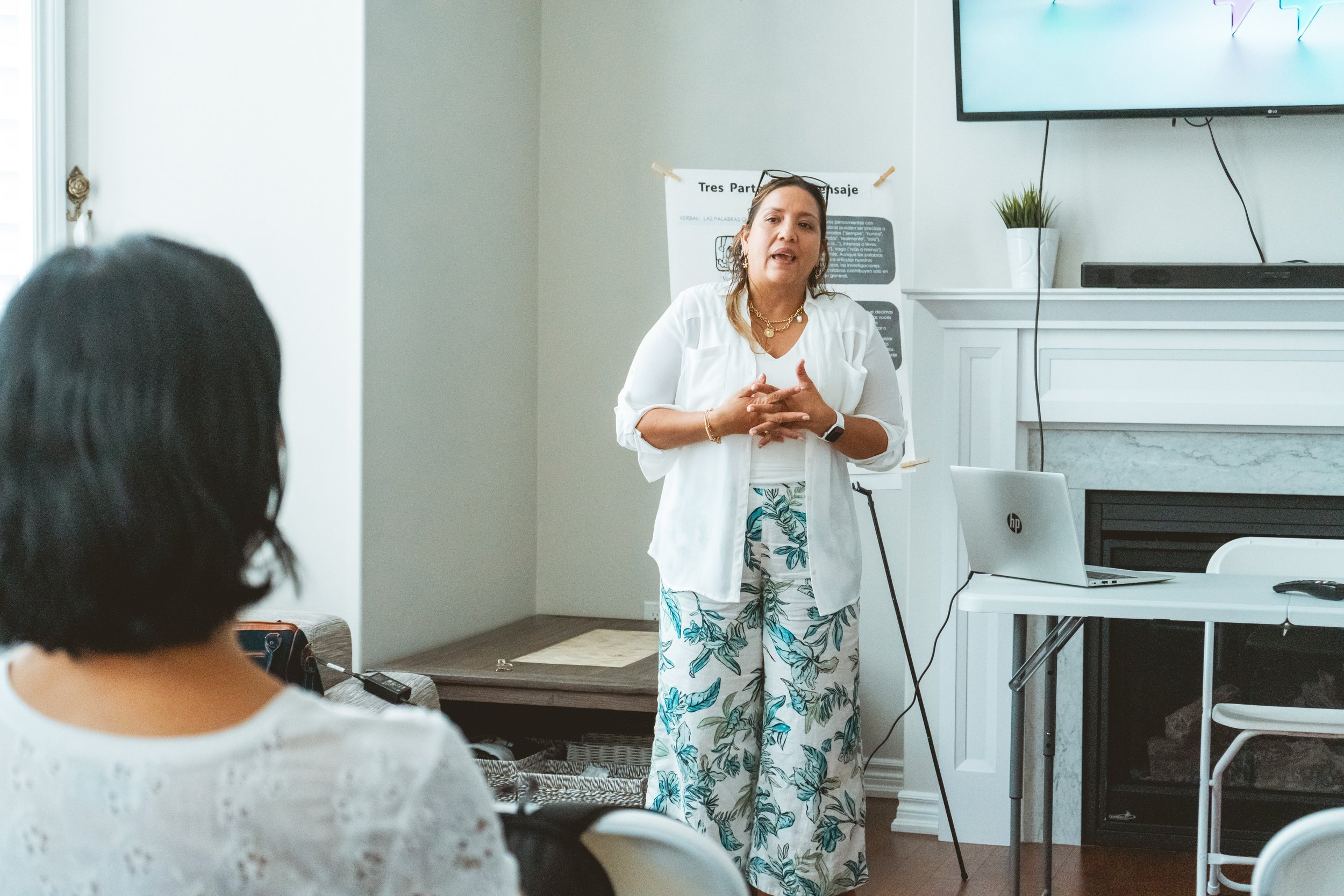 Woman giving a presentation in a home setting with a laptop and TV screen.
