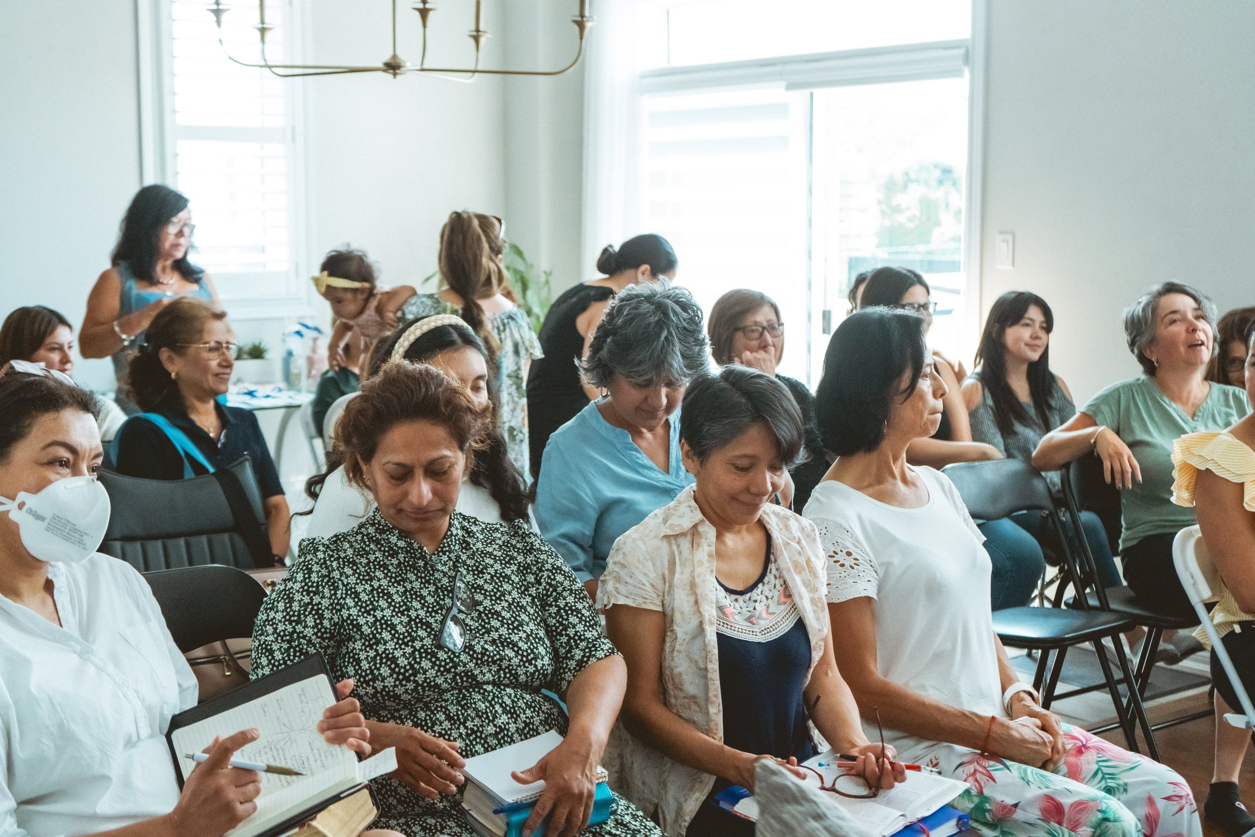 Group of diverse women sitting in a meeting room, some taking notes, others smiling and talking.