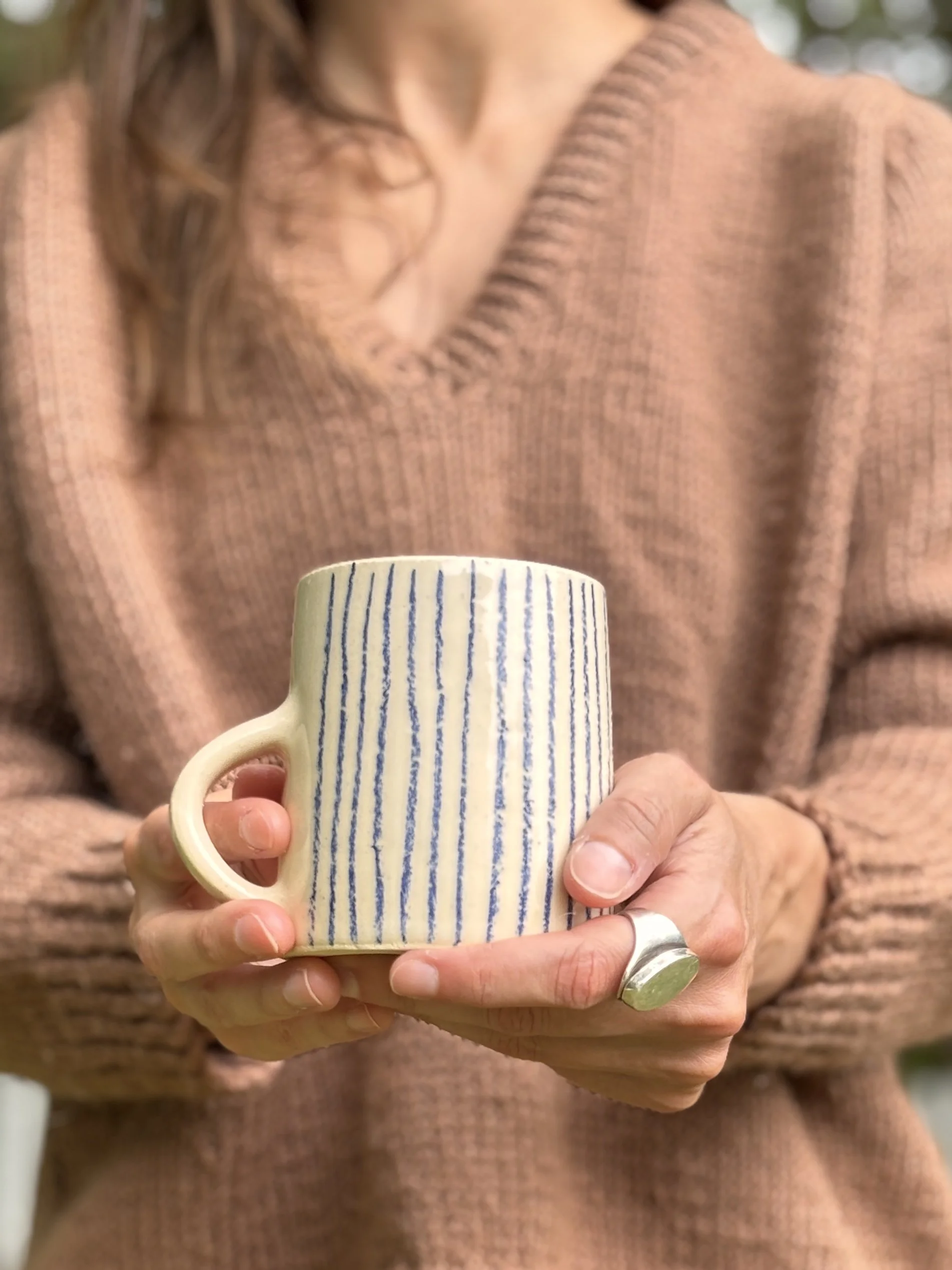 Person holding a ceramic mug with vertical blue stripes, wearing a copper-colored sweater.