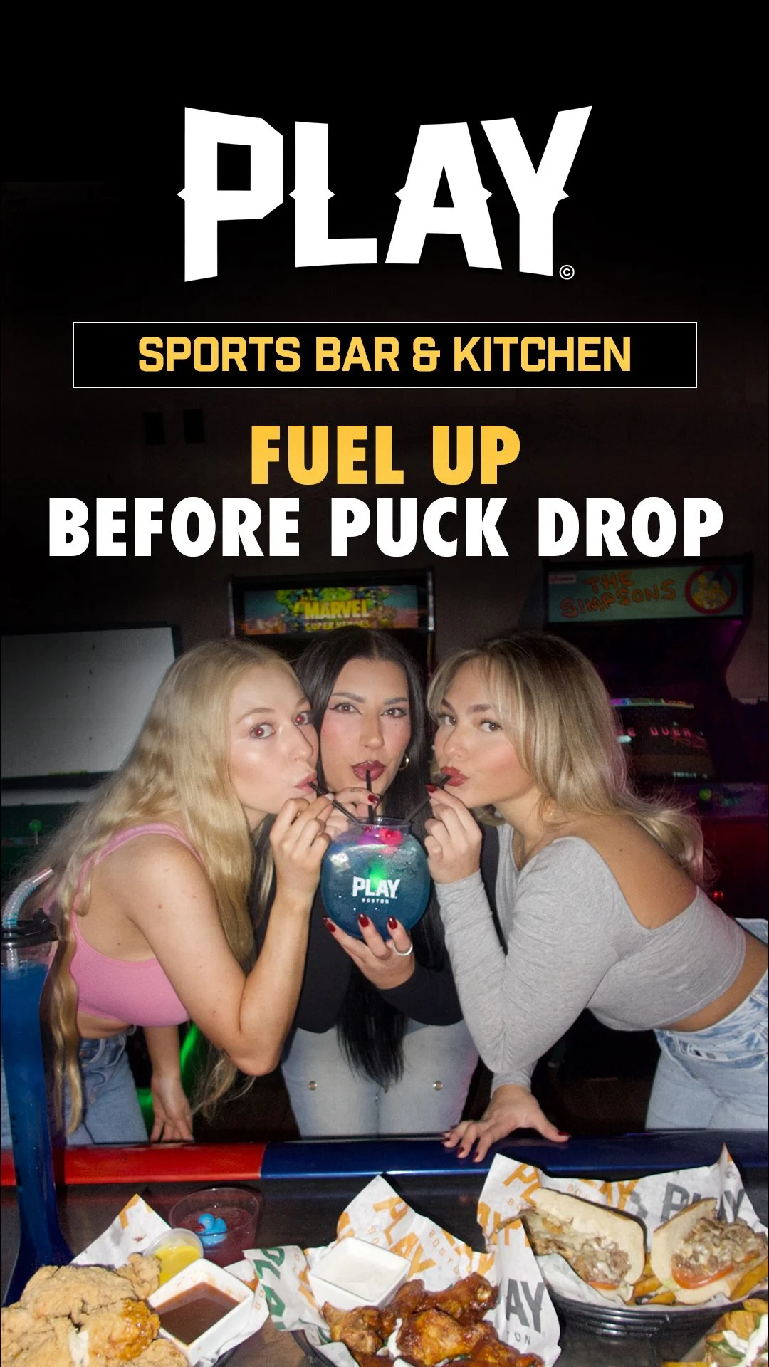 Three women at an arcade drinks alcohol from a large fish bowl with a straw, surrounded by plates of food, in front of arcade machines.