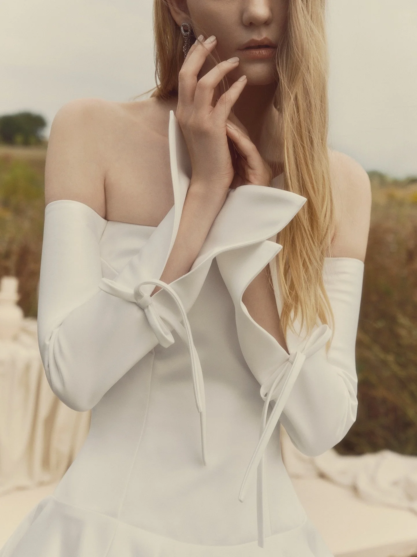 GRACE ✨🤍 Off-the-shoulder ballgown with voluminous proportions and long tailored sleeves. The flared sleeves open with a subtle slit, tied with a ribbon bow. Finished with pockets and buttons tracing the back to the hem- poised, dramatic, and quietl