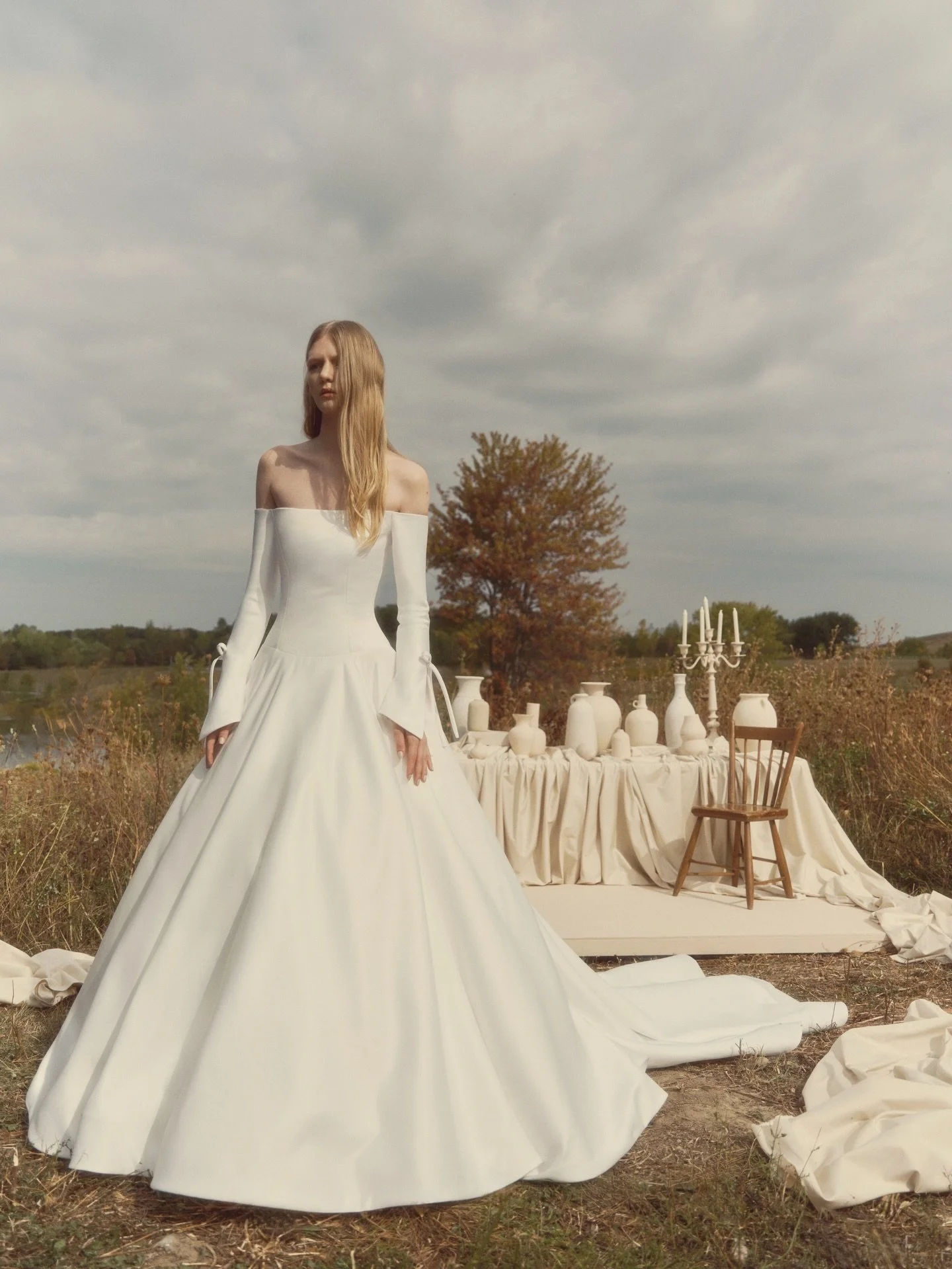 GRACE 🤍 Off-the-shoulder ballgown with voluminous proportions and long tailored sleeves. The flared sleeves open with a subtle slit, tied with a ribbon bow. Finished with pockets and buttons tracing the back to the hem- poised, dramatic, and quietly