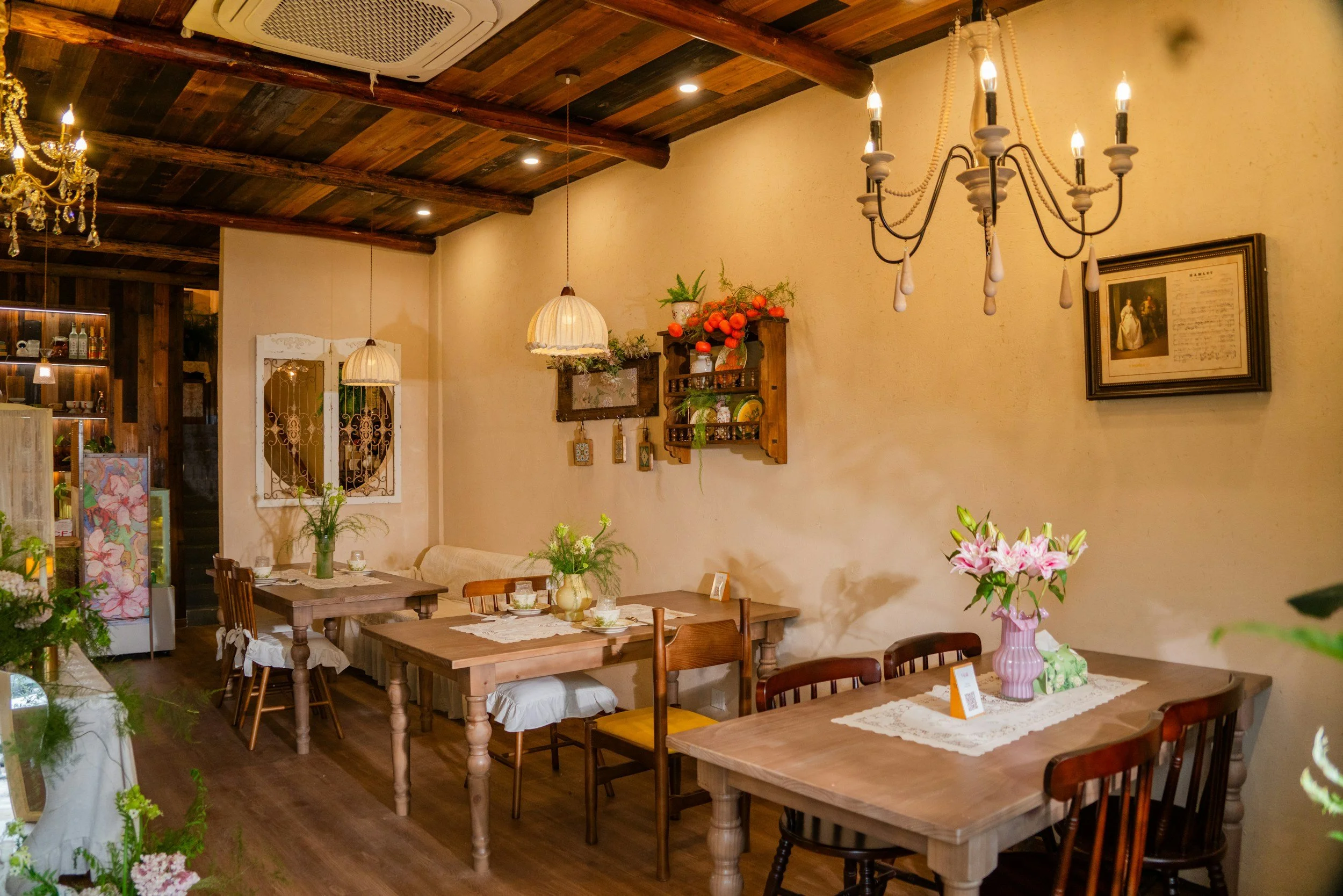 Cozy cafe with wooden tables and chairs, floral arrangements, vintage chandeliers and warm lighting, decorated with art and plants.