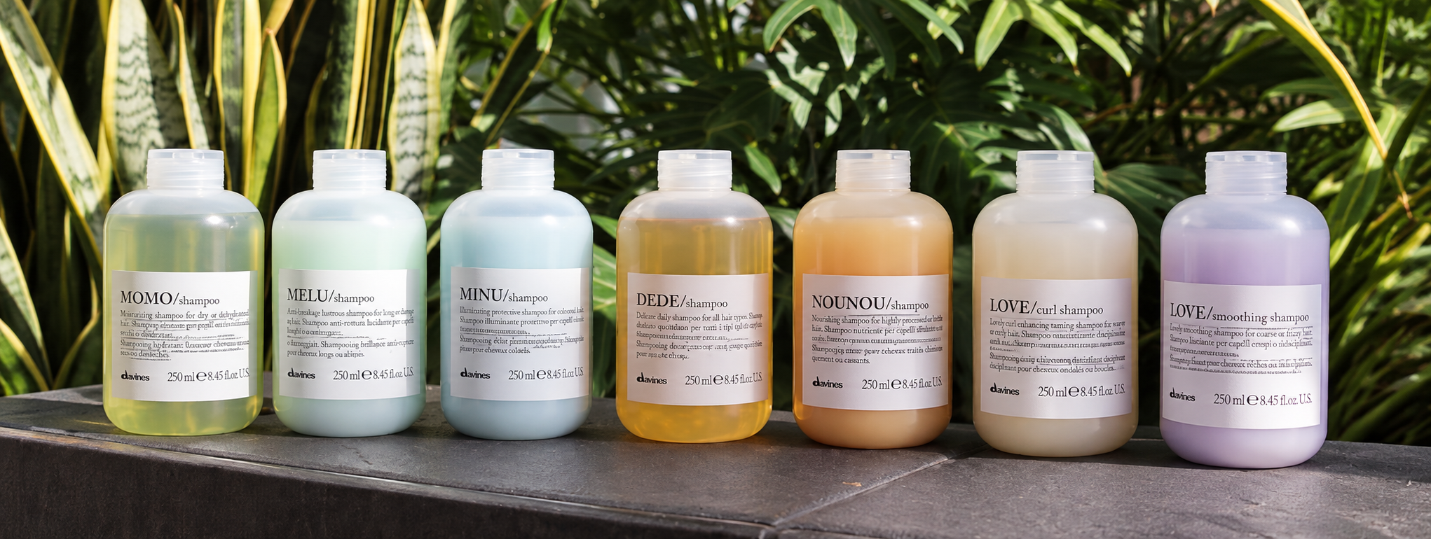Davines Essential Haircare shampoos displayed against lush green foliage.