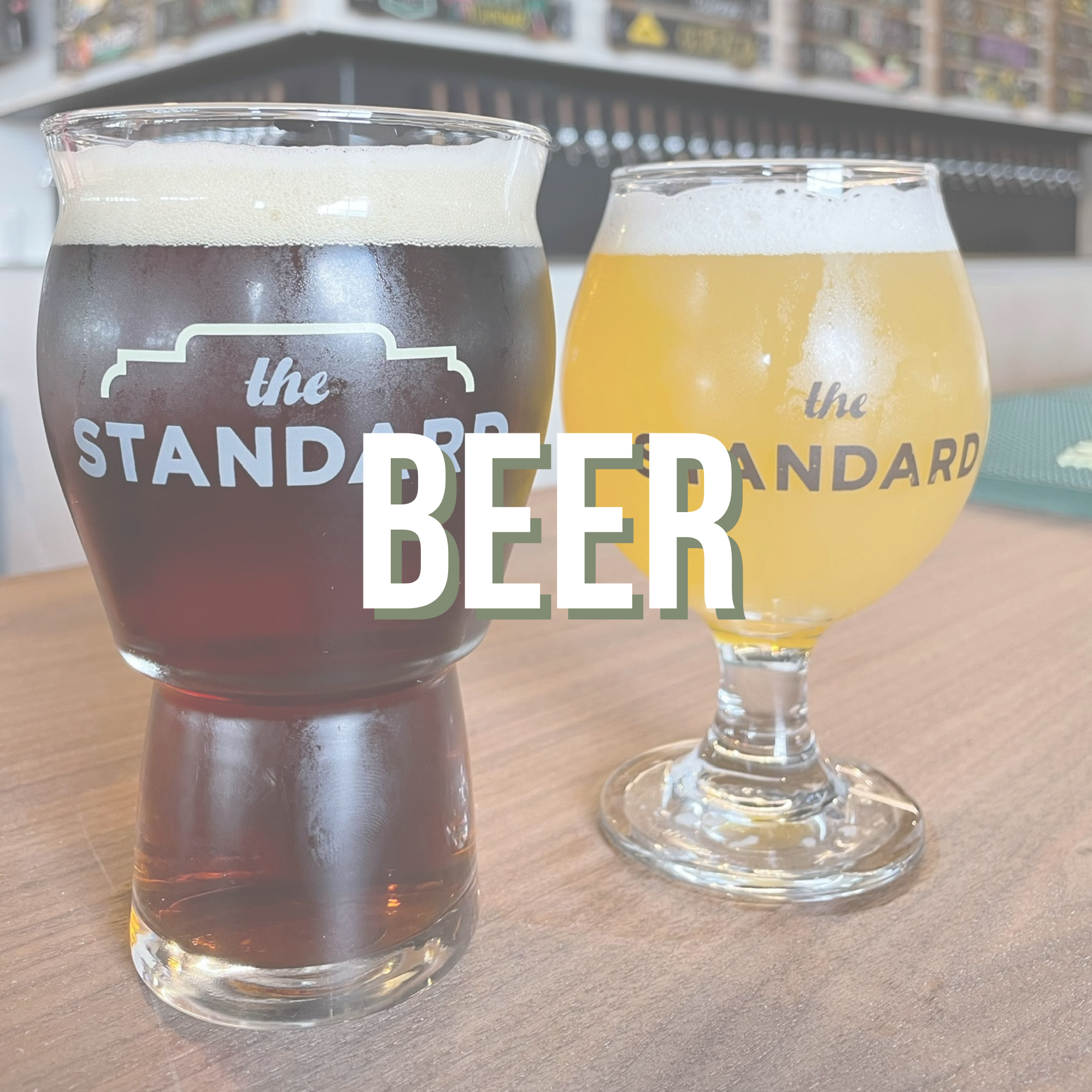 Two glasses of beer, one dark and one light, on a wooden table with the text "the STANDARD BEER" overlaying the image.