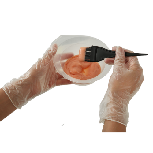 Person wearing gloves mixing peach-colored substance in a white bowl with a brush.