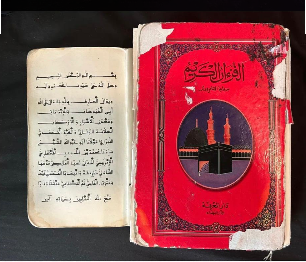 A worn, open Arabic book on the left and a damaged red Quran cover on the right with an illustration of the Kaaba and minarets.