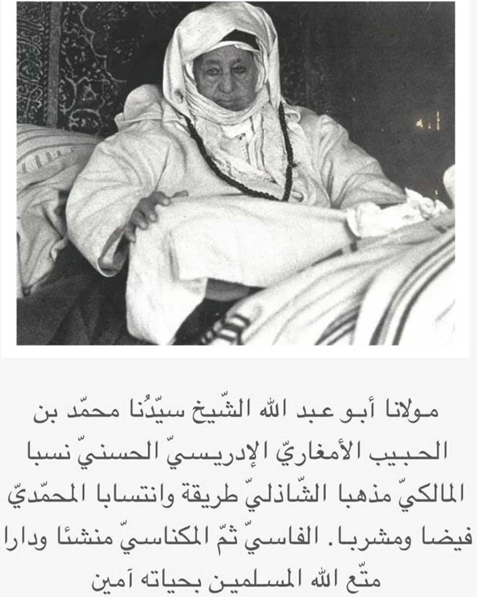 A black and white photo of a man dressed in traditional Middle Eastern attire, sitting and smiling, with Arabic script beneath the image.