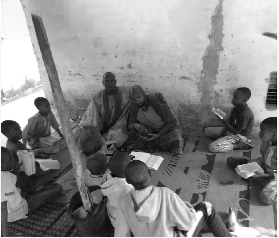 A group of children and two adults sitting on the floor in a room, engaged in reading or studying.