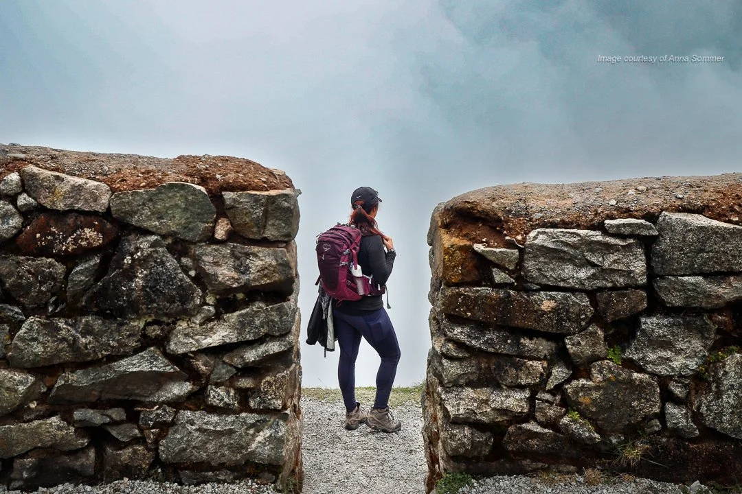 Lona Downs stands at the ancient Runkuraqay Ruins, overlooking a misty valley on the Inca Trail. This shot was captured with a Canon EOS 5D Mark IV by Anna Sommer, highlighting the mystical atmosphere of the Andes