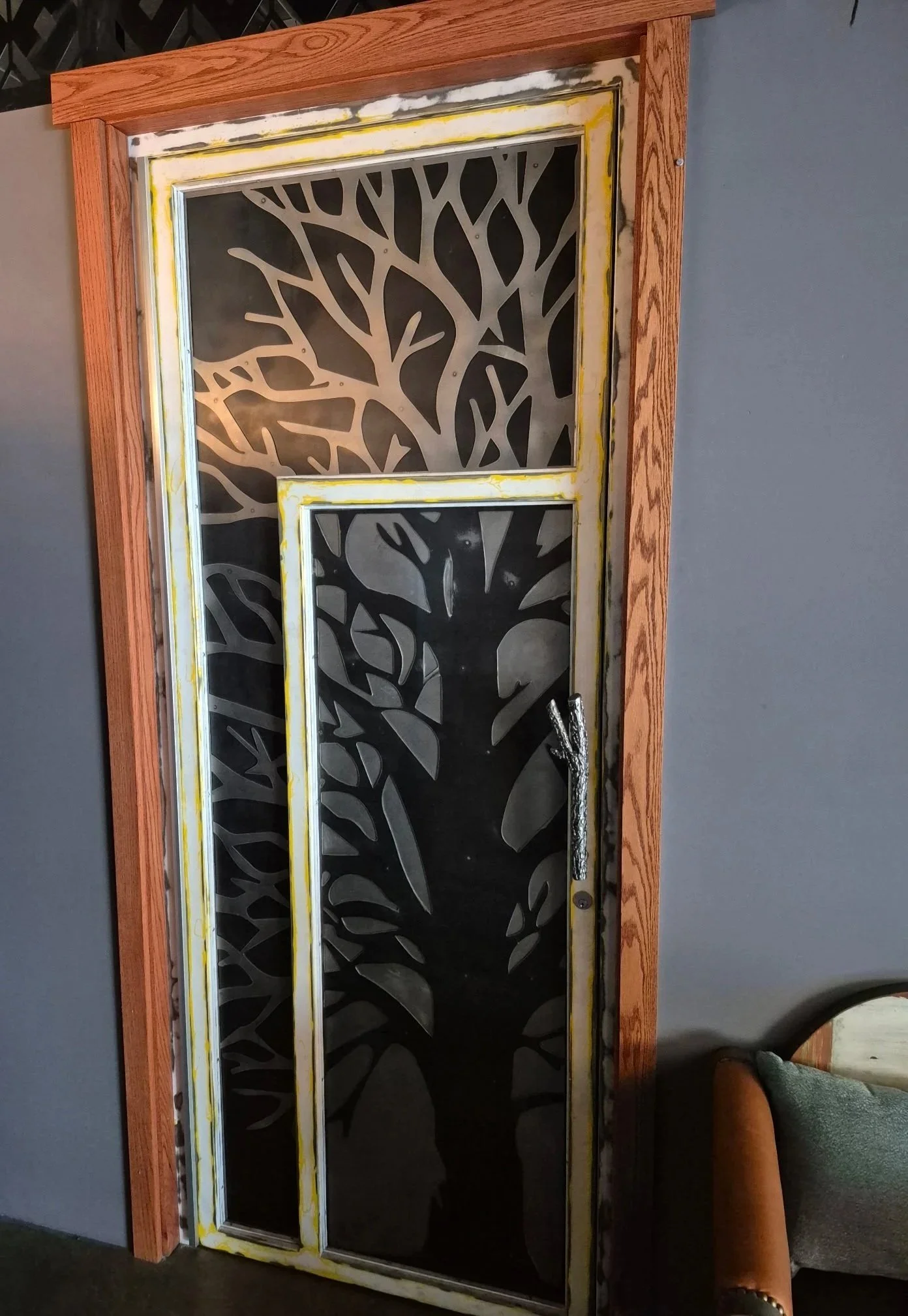 Custom fabricated metal panel with tree design made into a custom door frame. The door has a custom fabricated door pull in the shape of a tree branch