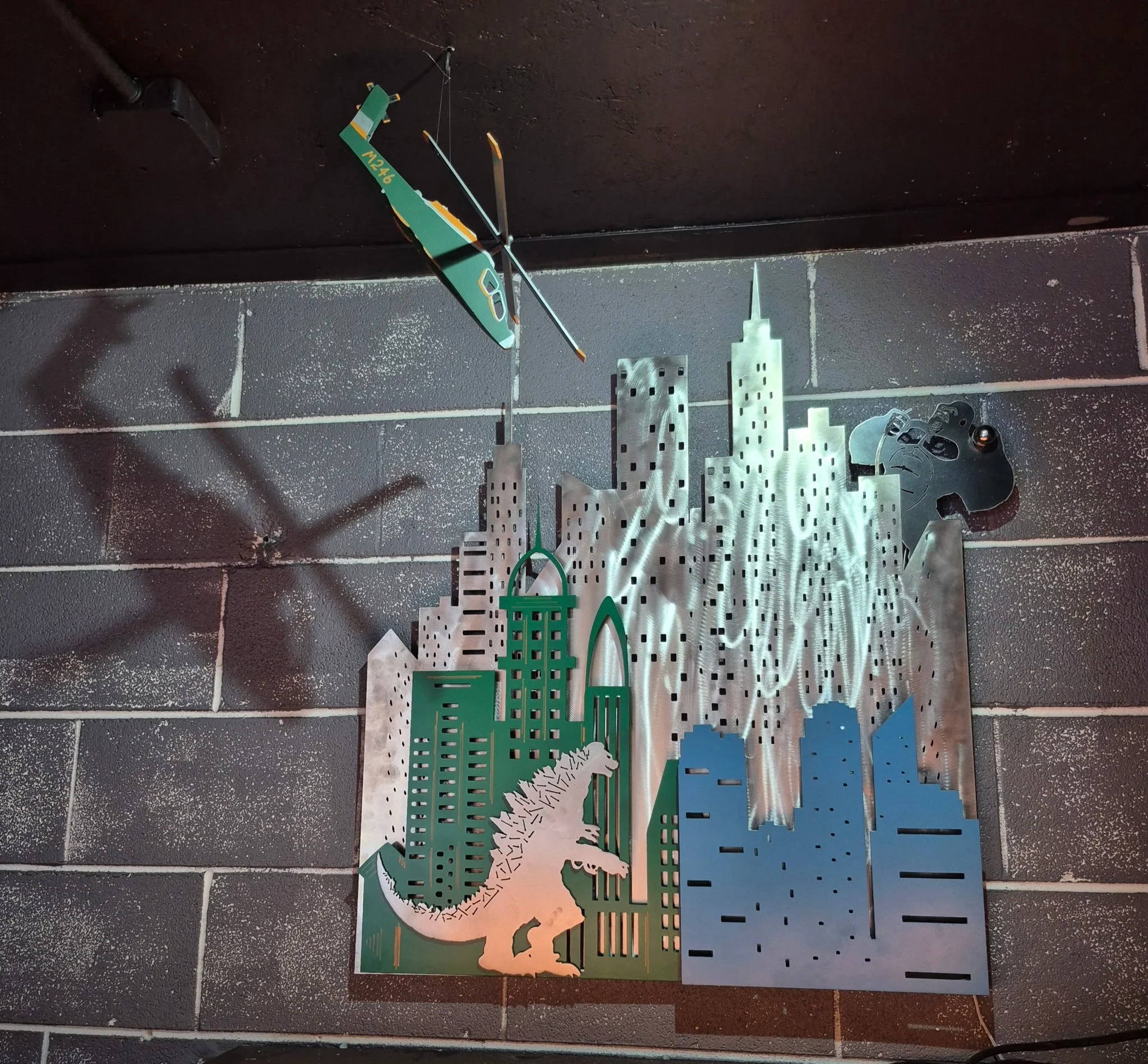 Custom metal layered sign in the shape of a city with King Kong, Godzilla and a fabricated metal helicopter replica above
