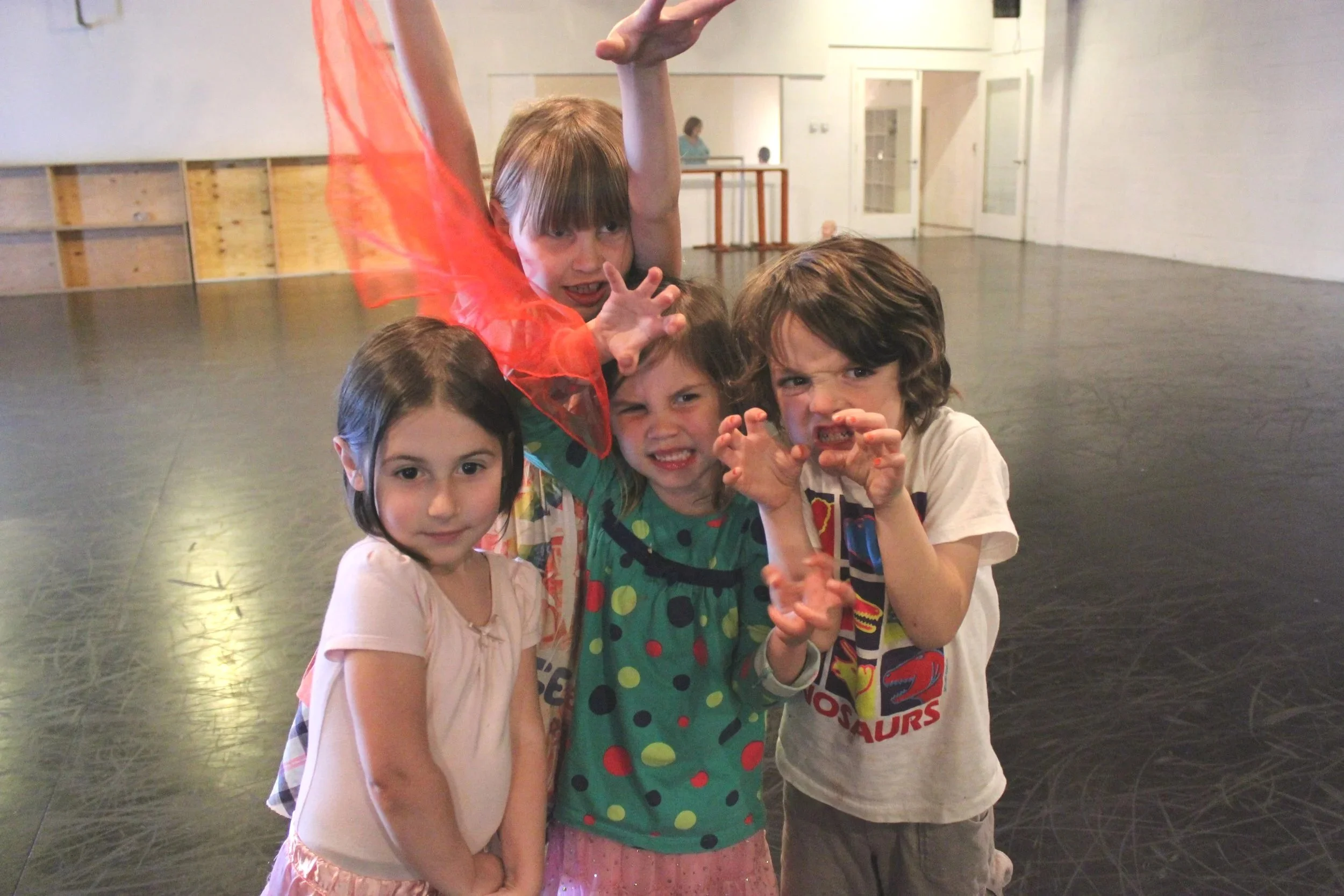 Four children posing playfully indoors. Four girls standing closely, making funny faces, wearing casual or costume-like clothing.