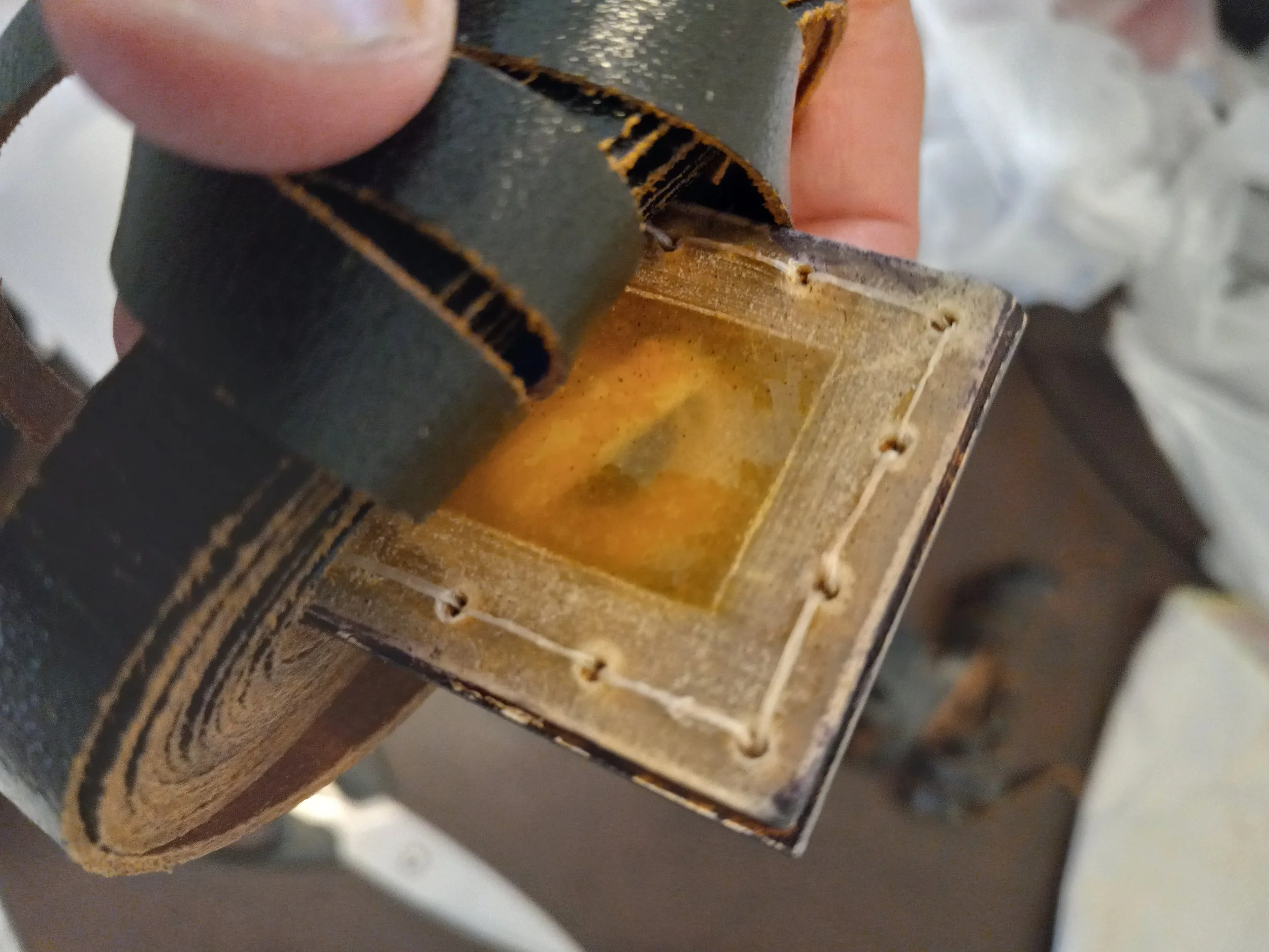 Close-up of a person's hand holding a small square component with a burnt or damaged surface, possibly a circuit or electronic part.