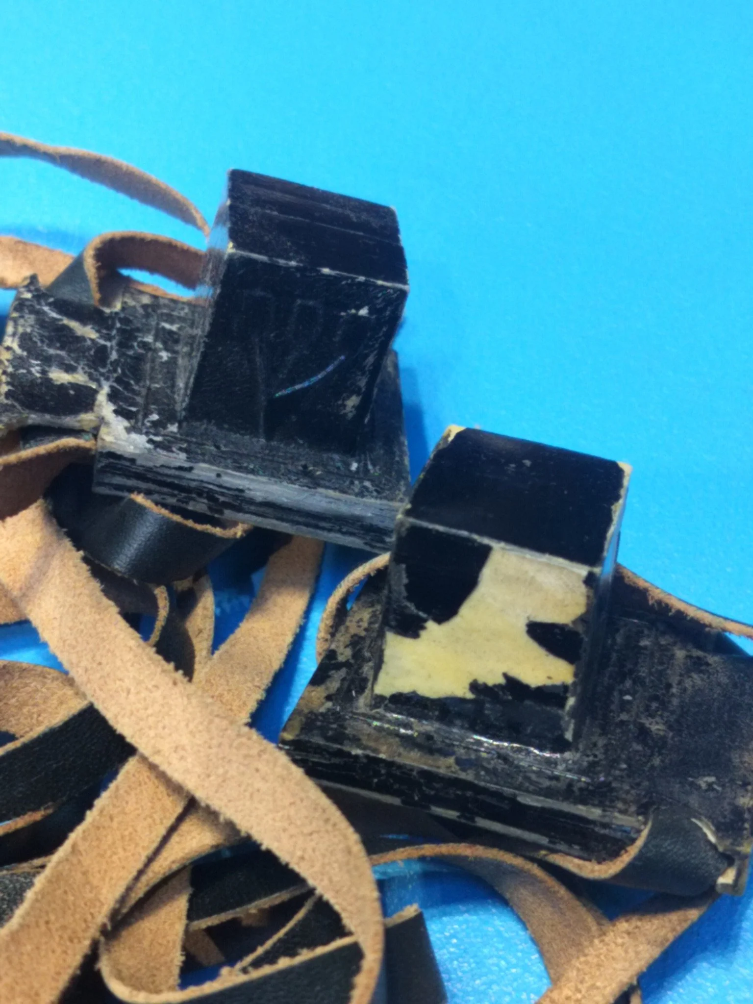 Close-up of a pair of black leather boxing gloves with frayed laces and worn surface, resting on a blue background.