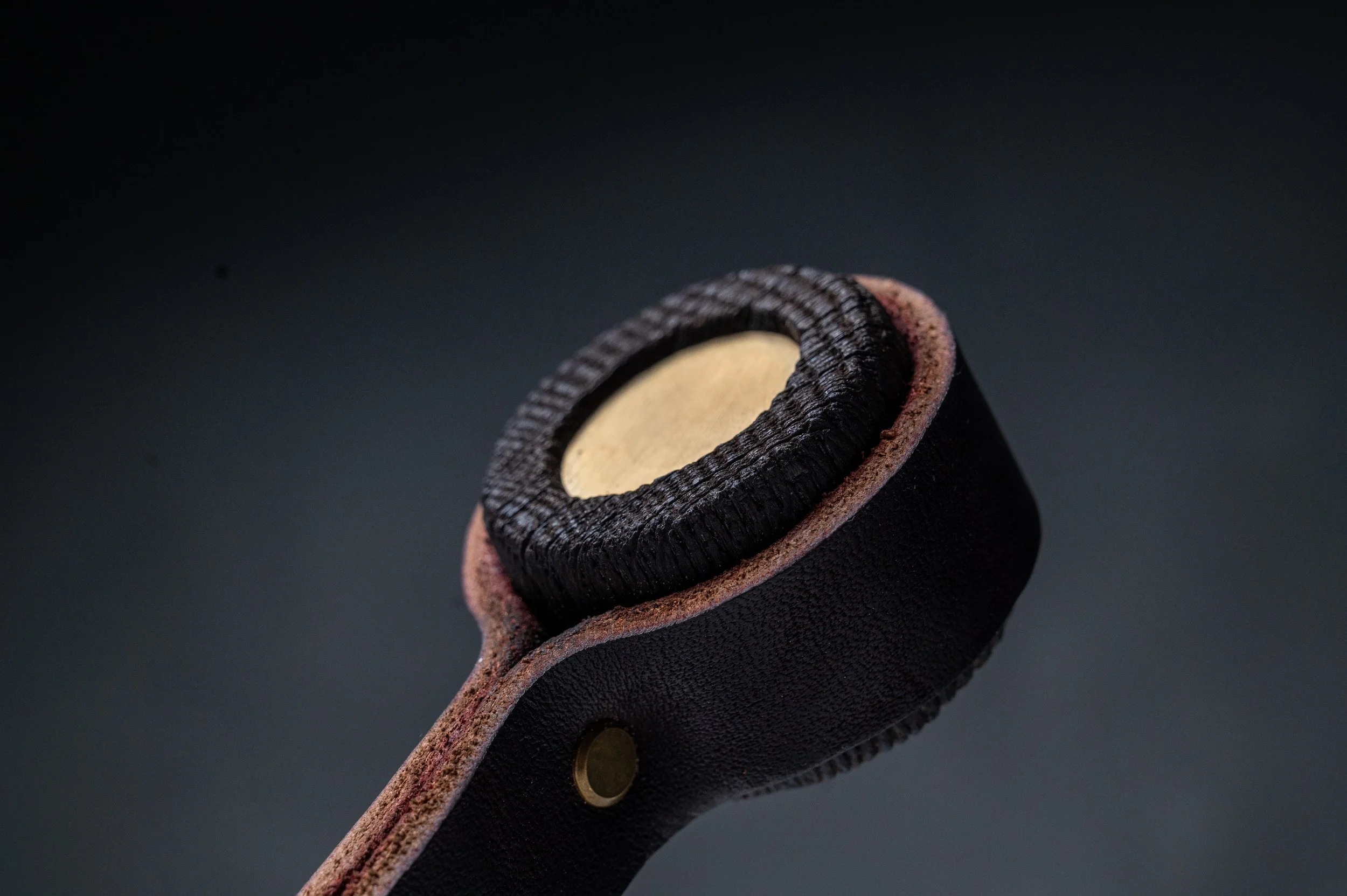 Close-up of a black leather strap with a circular cutout, showing the inner padding and button detail, against a dark background.