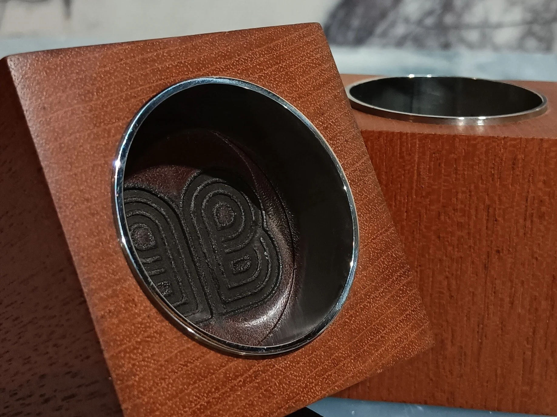 Close-up of a square shaped tealight holder in brown wood with a polished steel inner circle and bottom finished with a leather  and stamped with the company bluntas bespoke logo