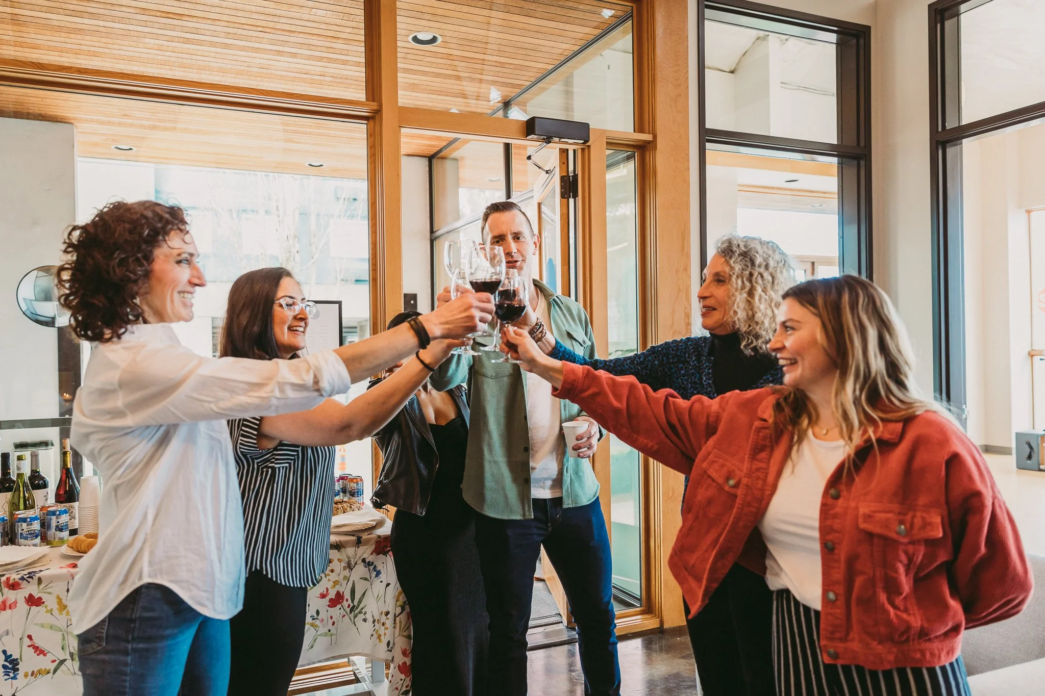 A group of smiling people clinking wine glasses together on opening day