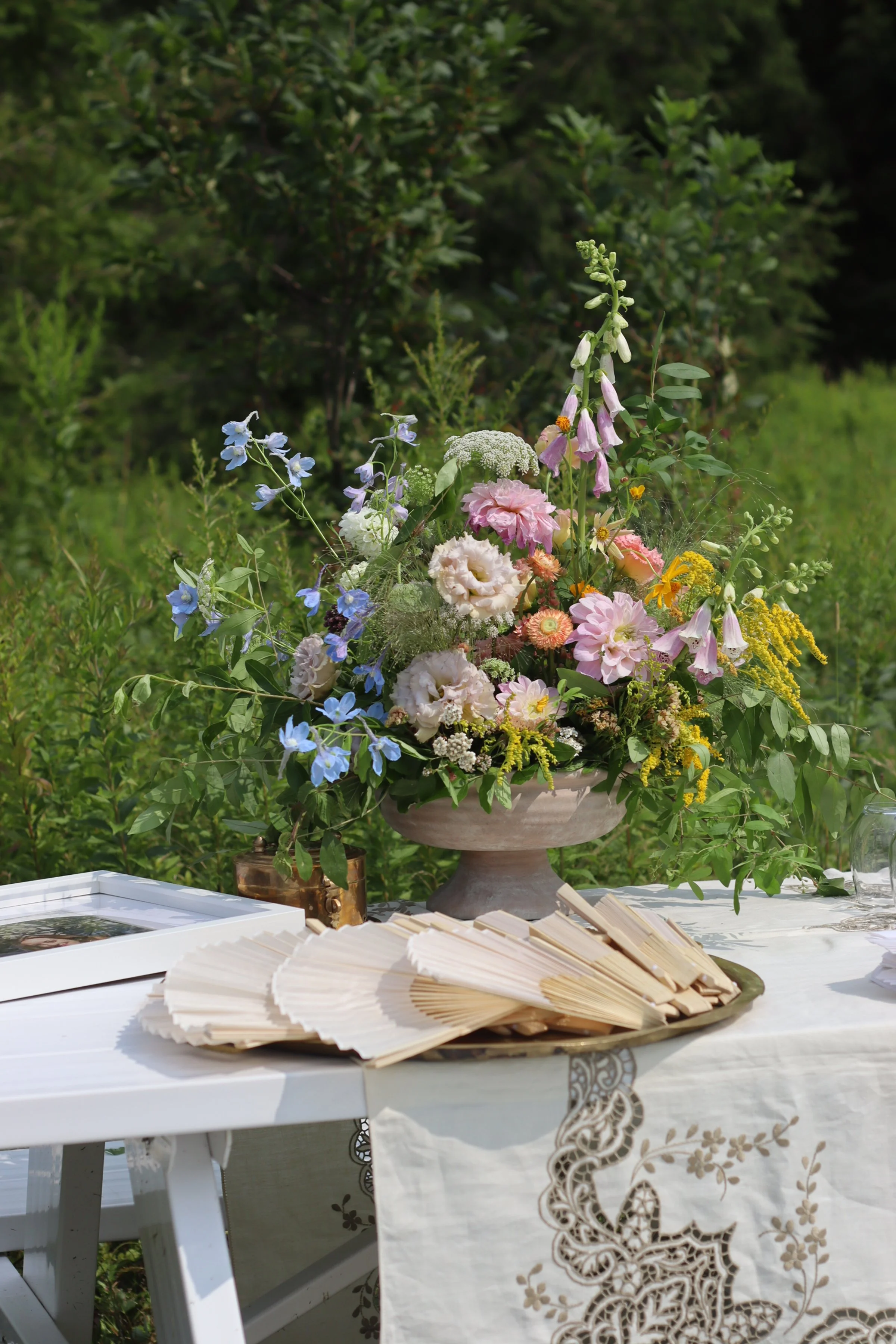 Summer wedding welcome floral arrangement.  Colorful flowers in ceramic urn on picnic table. Outdoor wedding, Hudson Valley floral designer. New York florist.